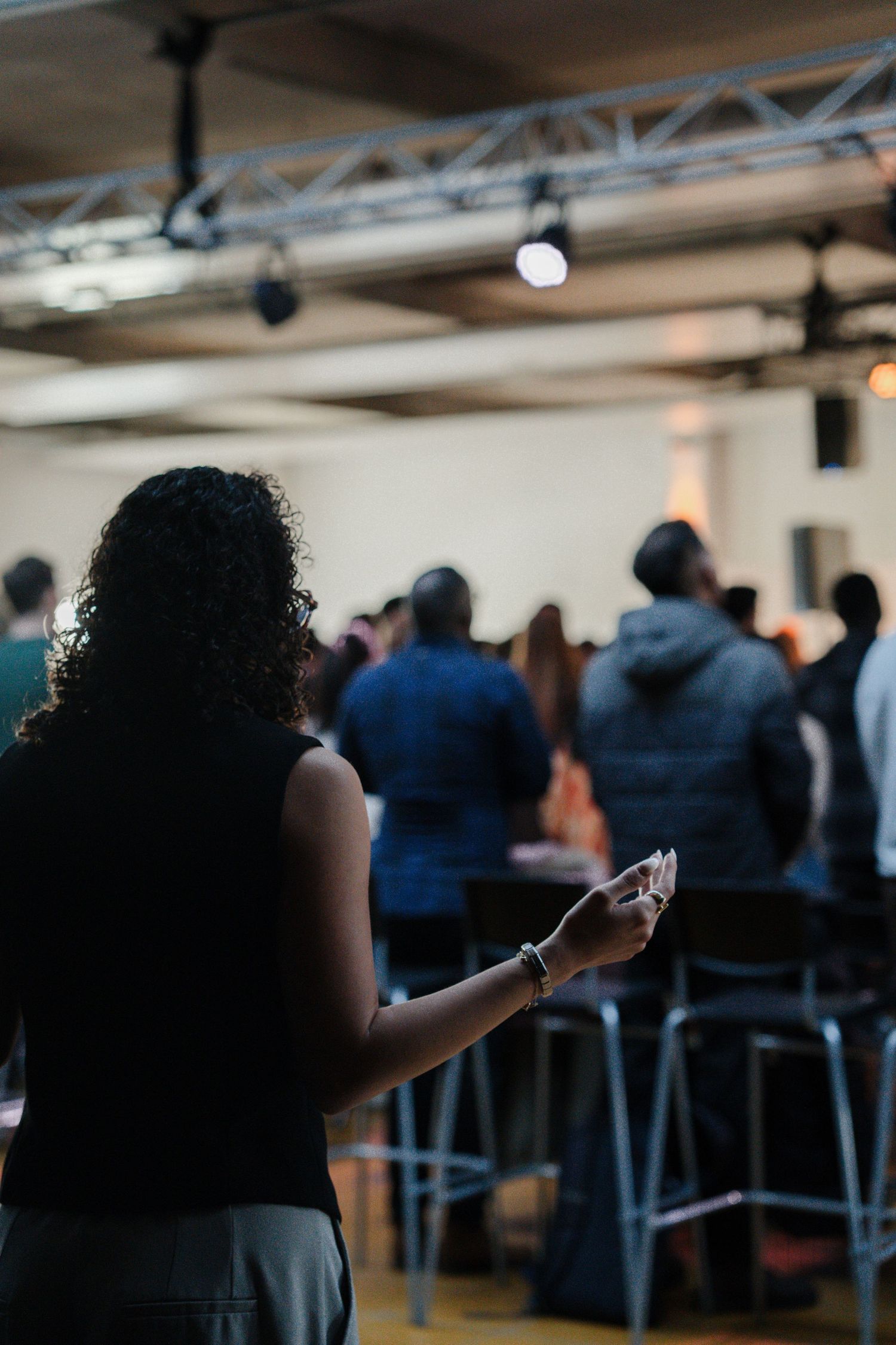 Curly-haired woman holding papers stands among a congregation during a church worship service.