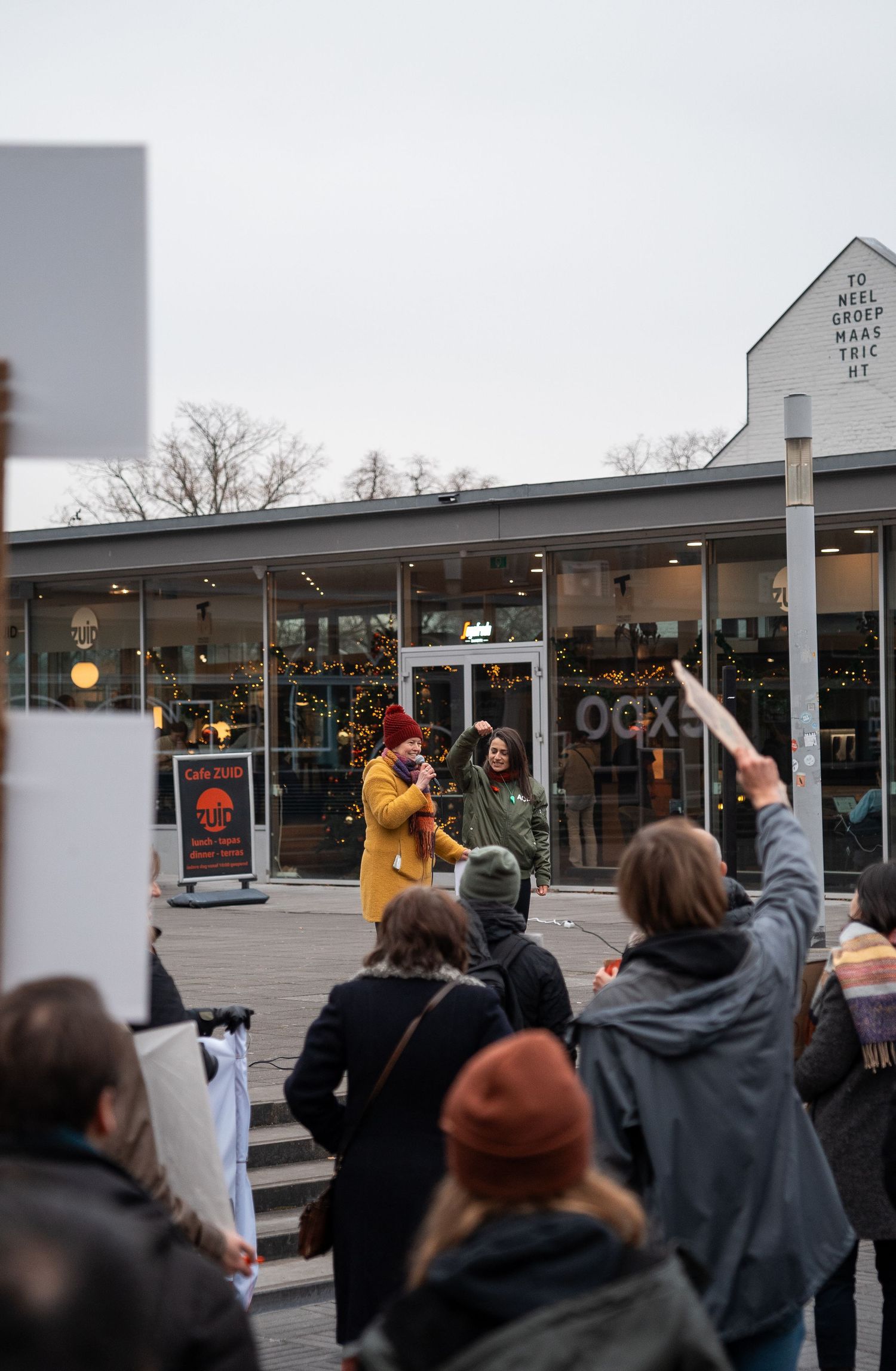 Two speakers address a crowd of protesters outside a glass building during a demonstration.