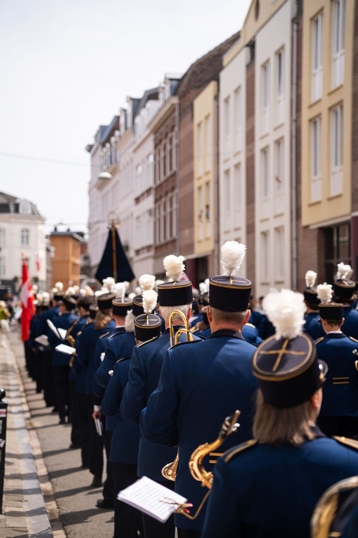 Rear view of marching band in blue uniforms with white plumes parading down a city street.