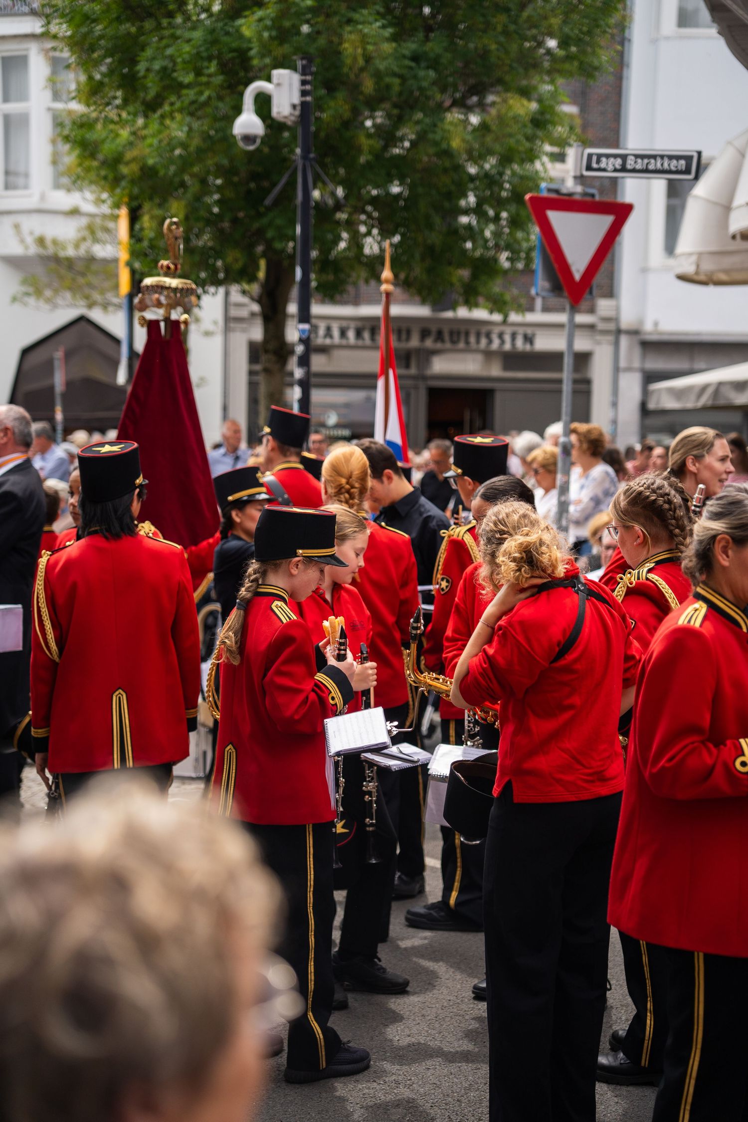 Marching band members in red uniforms perform during a street parade in a European town.