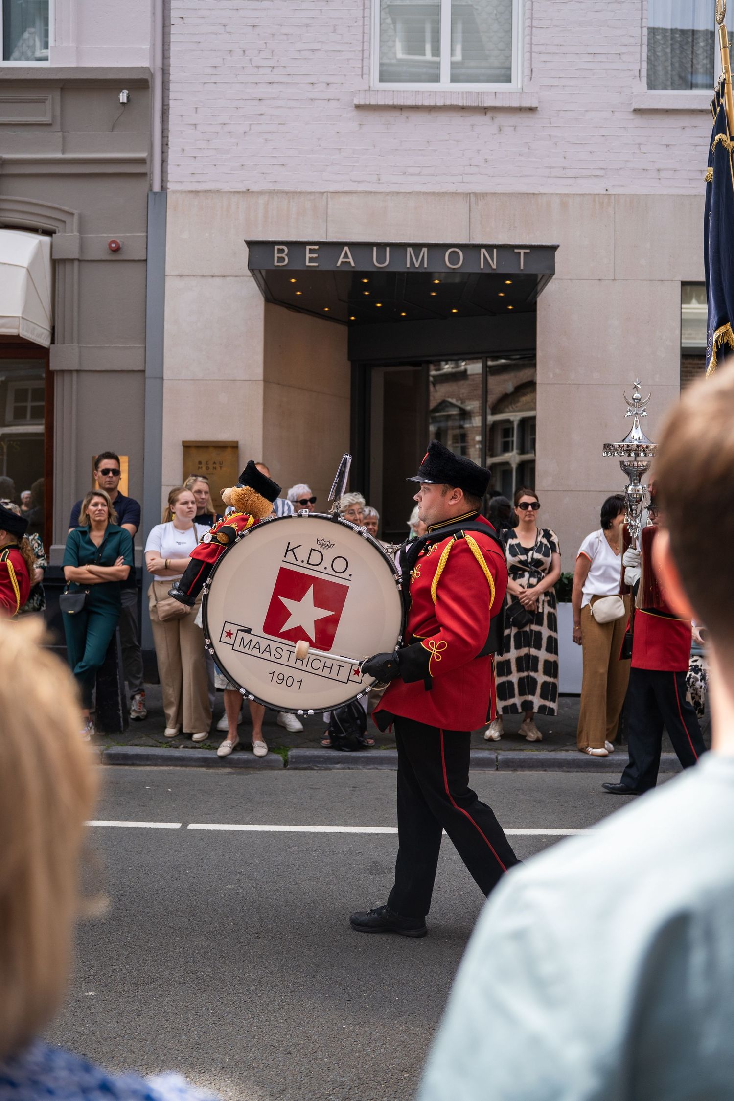 Musician in red uniform plays bass drum marked K.D.O. Maastricht 1901 in street parade.