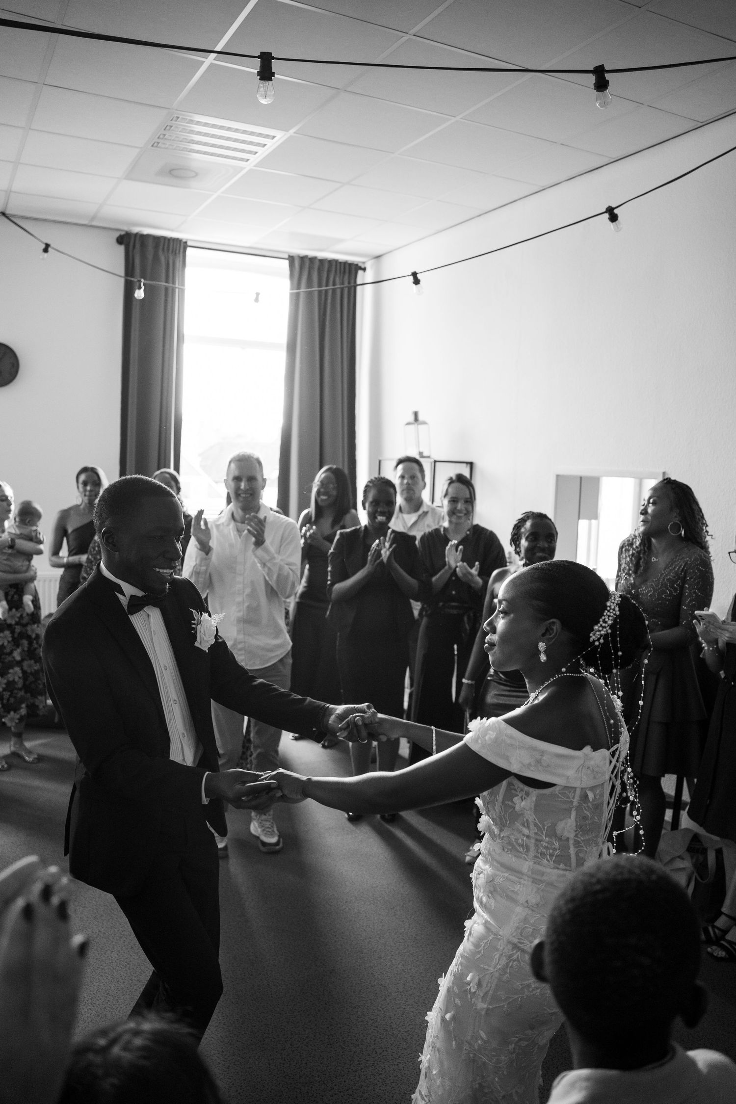 Black and white photo of newlyweds sharing first dance surrounded by clapping guests.
