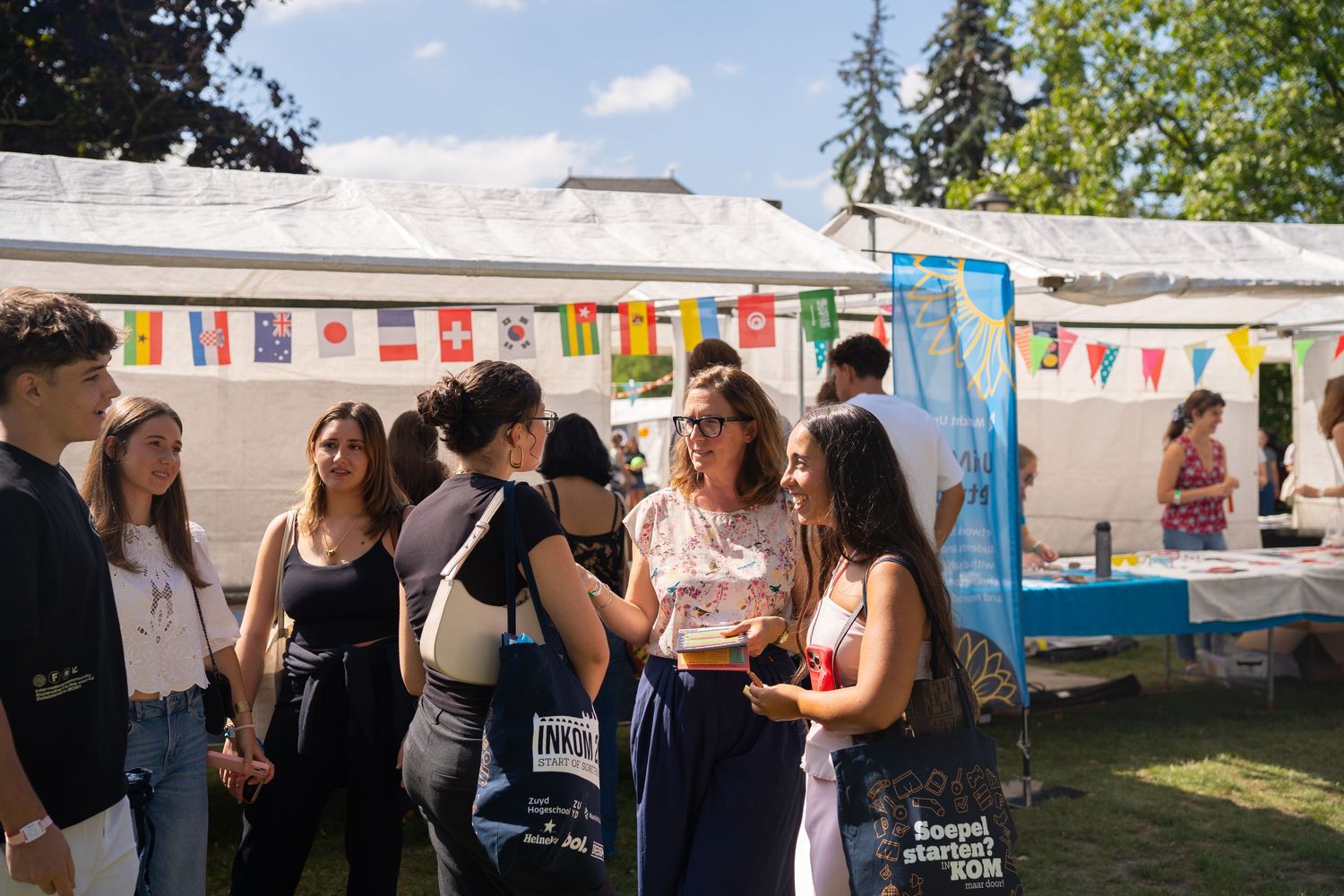 Students mingle at an outdoor international university fair with colorful country flags and event banners.