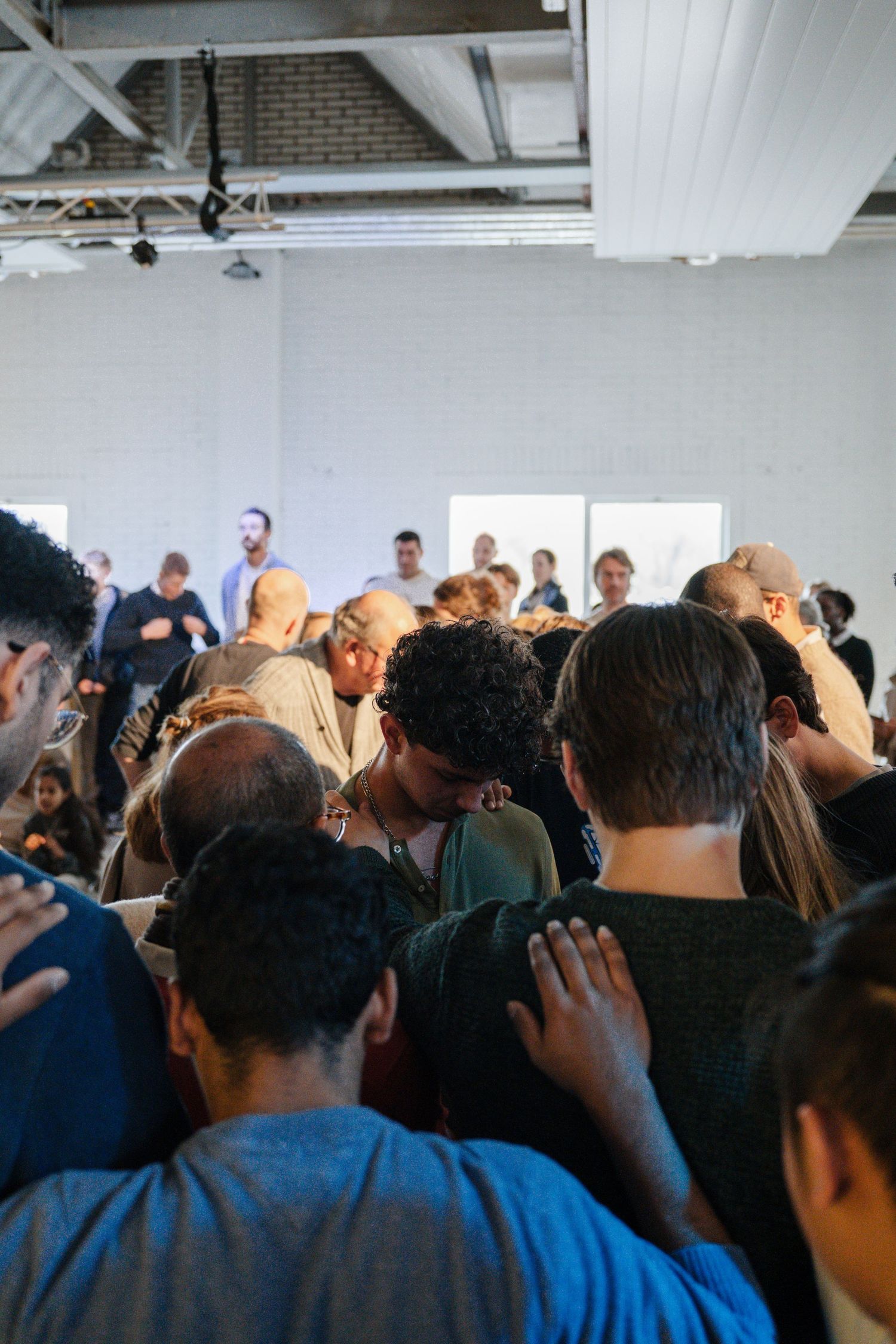 Diverse crowd of people gathered closely together in prayer at an indoor church service event.