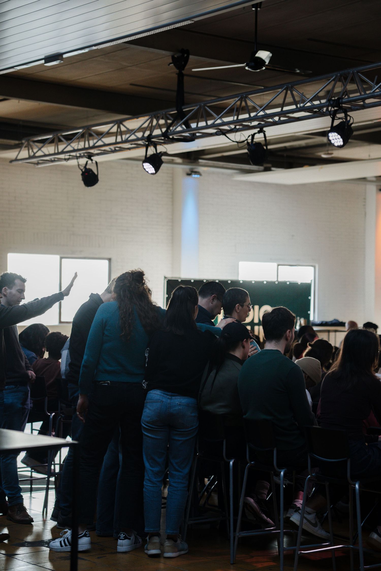 Group of young people gathered in prayer circle during a church service in a modern worship space.