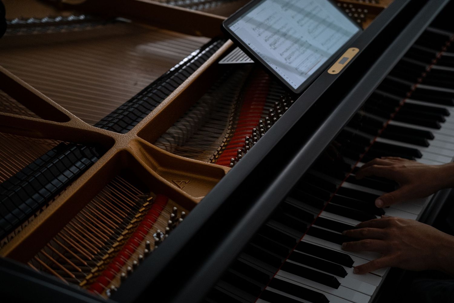 Overhead view of hands playing a grand piano with sheet music visible on stand.