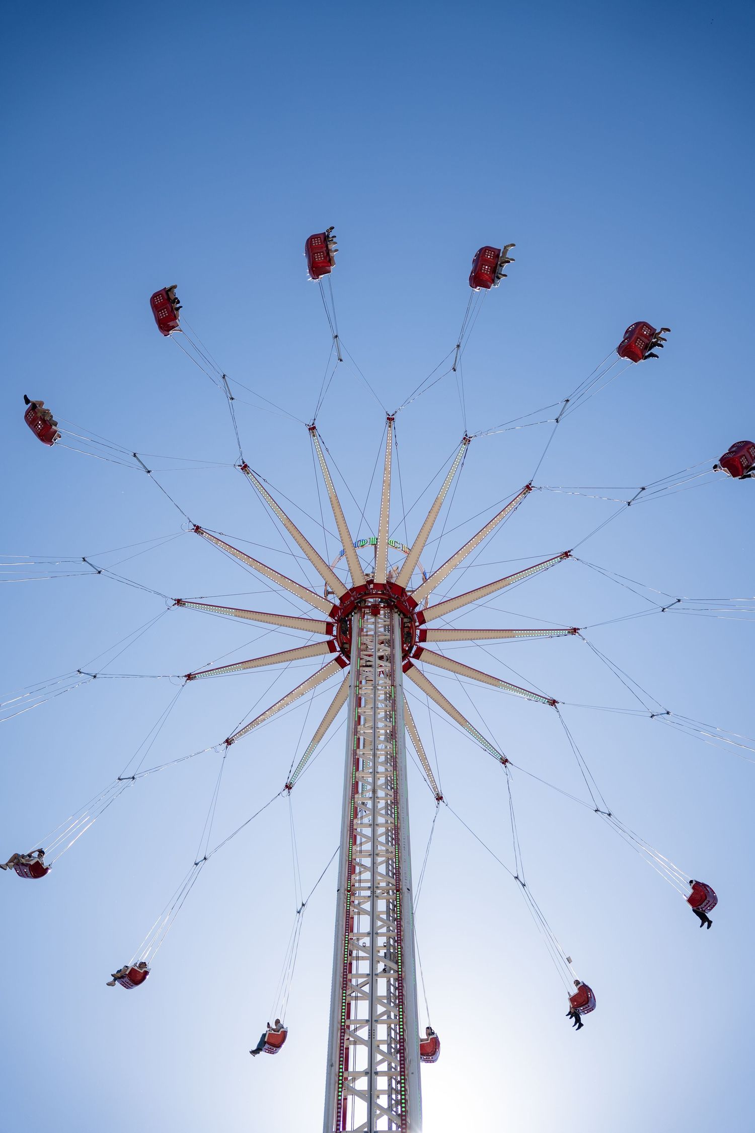 Low-angle view of a towering chain swing carousel ride with riders suspended against a clear blue sky.