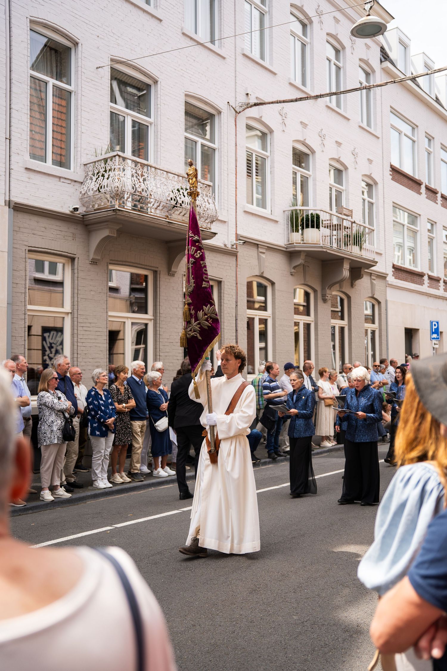 Robed participant carries ornate purple banner with golden finial in a religious street procession.