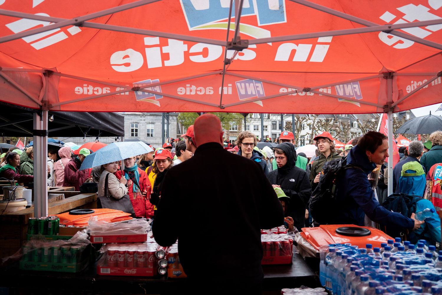 People gathering under a red FNV in Actie union tent at a protest rally with supplies on tables.