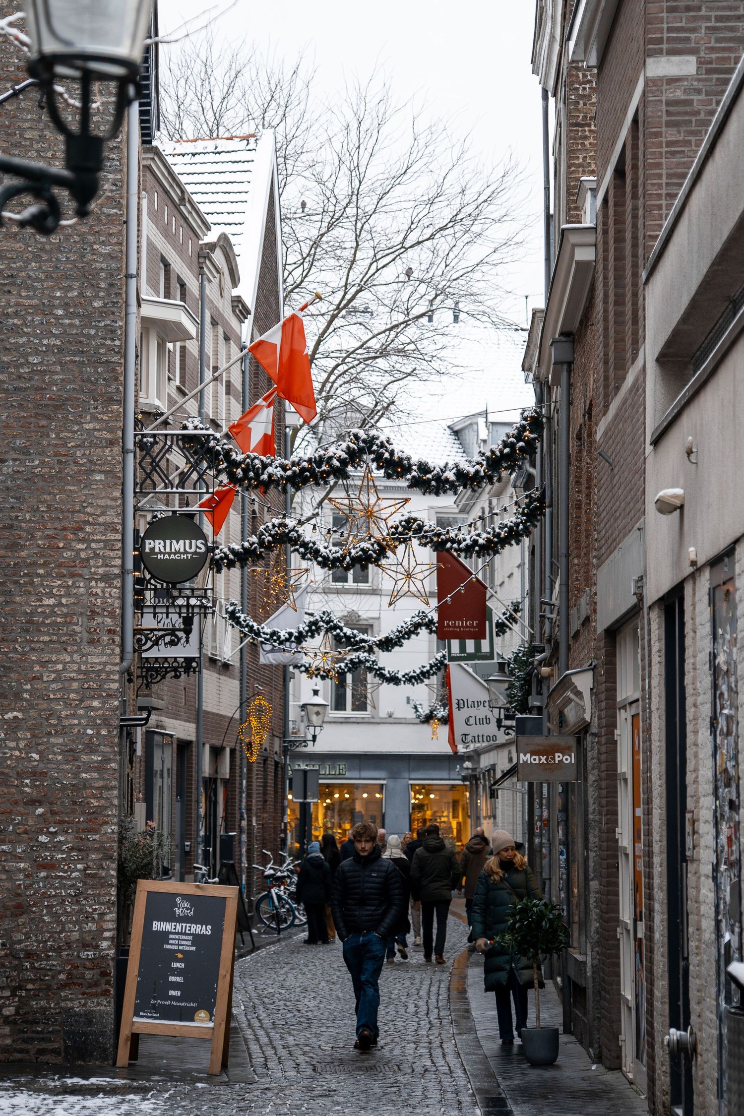 Festive Christmas-decorated cobblestone alley with garlands and red bows in a historic European city.