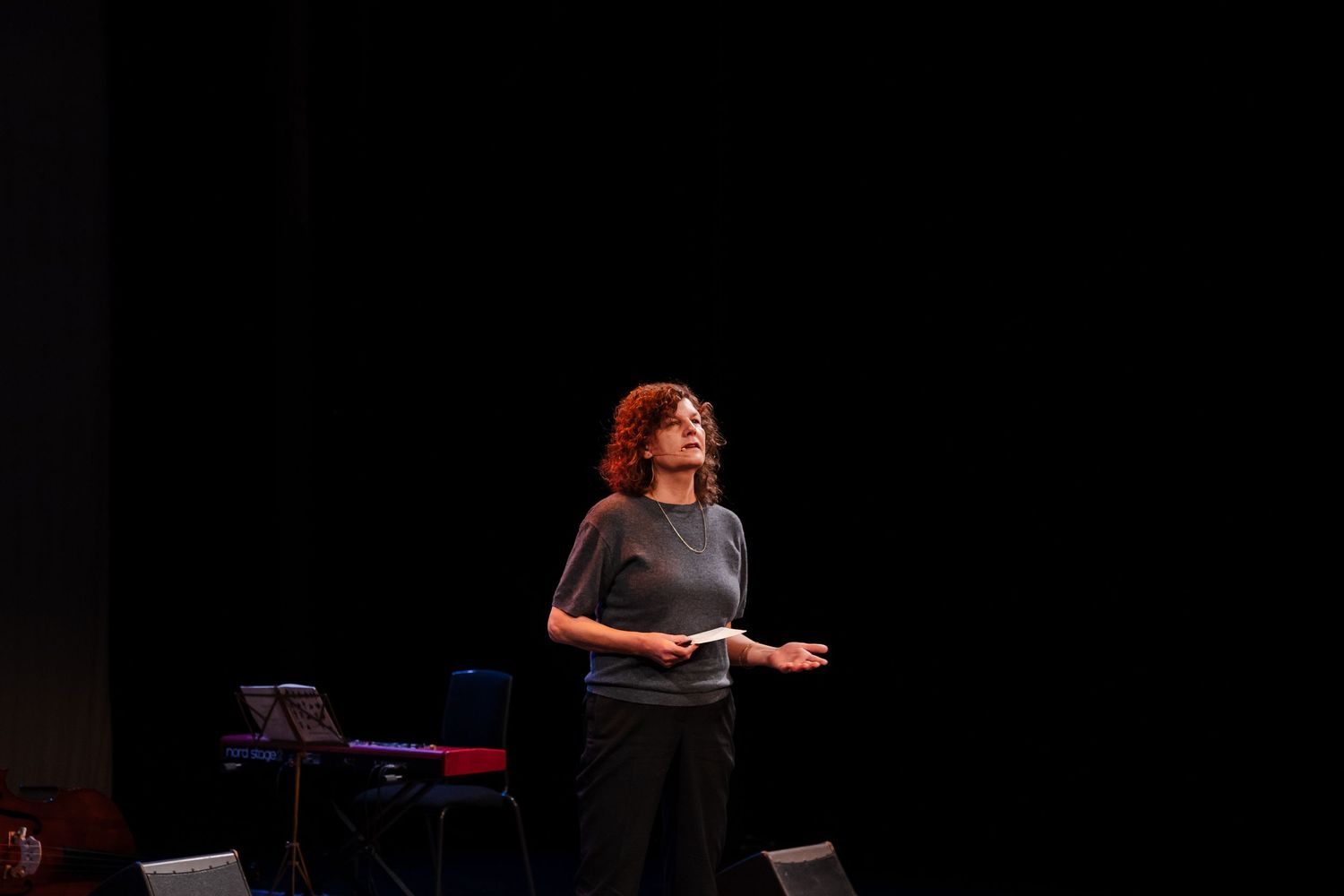 Female speaker with curly red hair presenting on dark theater stage.