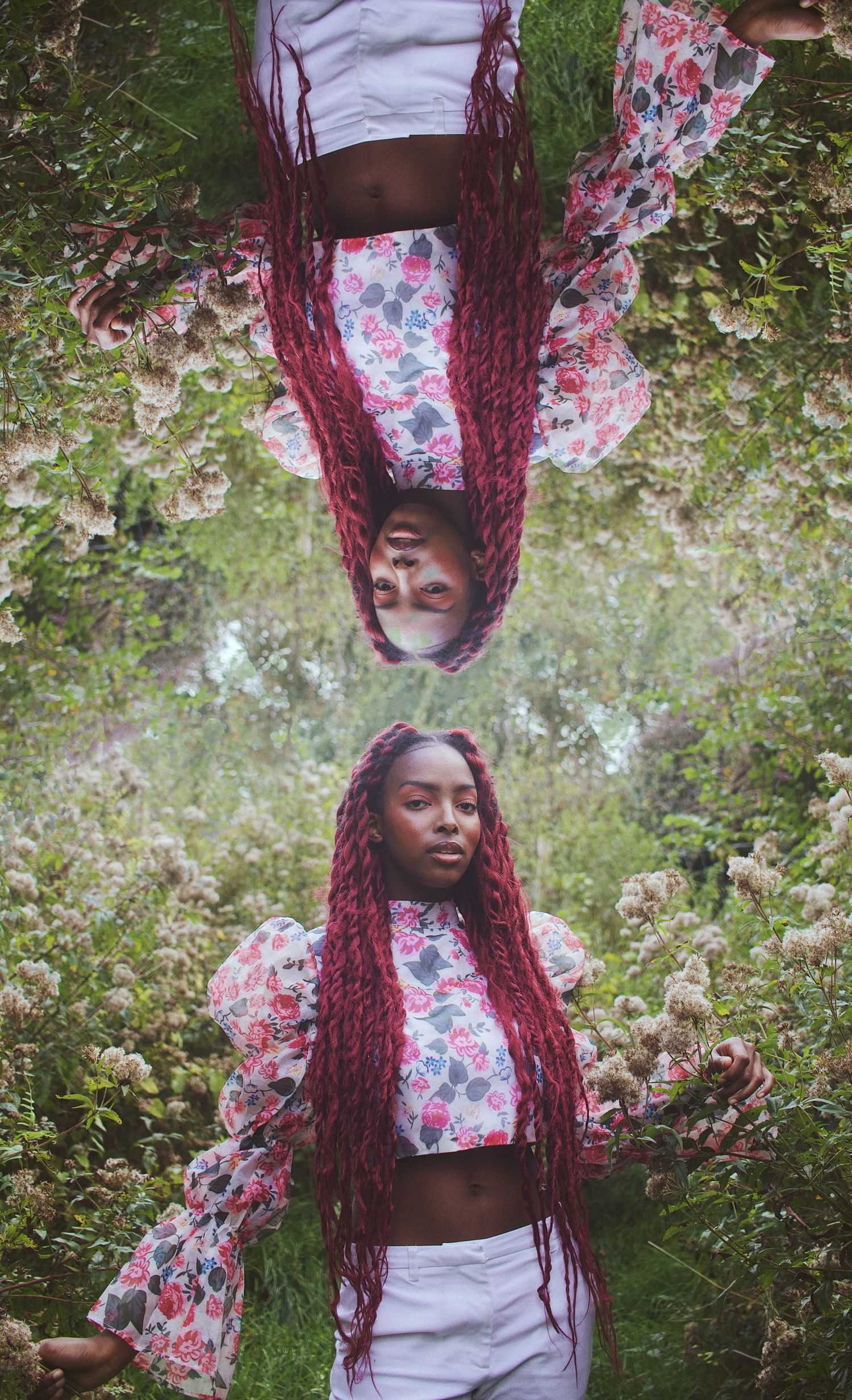 Creative mirrored portrait of woman with red braids in floral outfit among wildflowers.