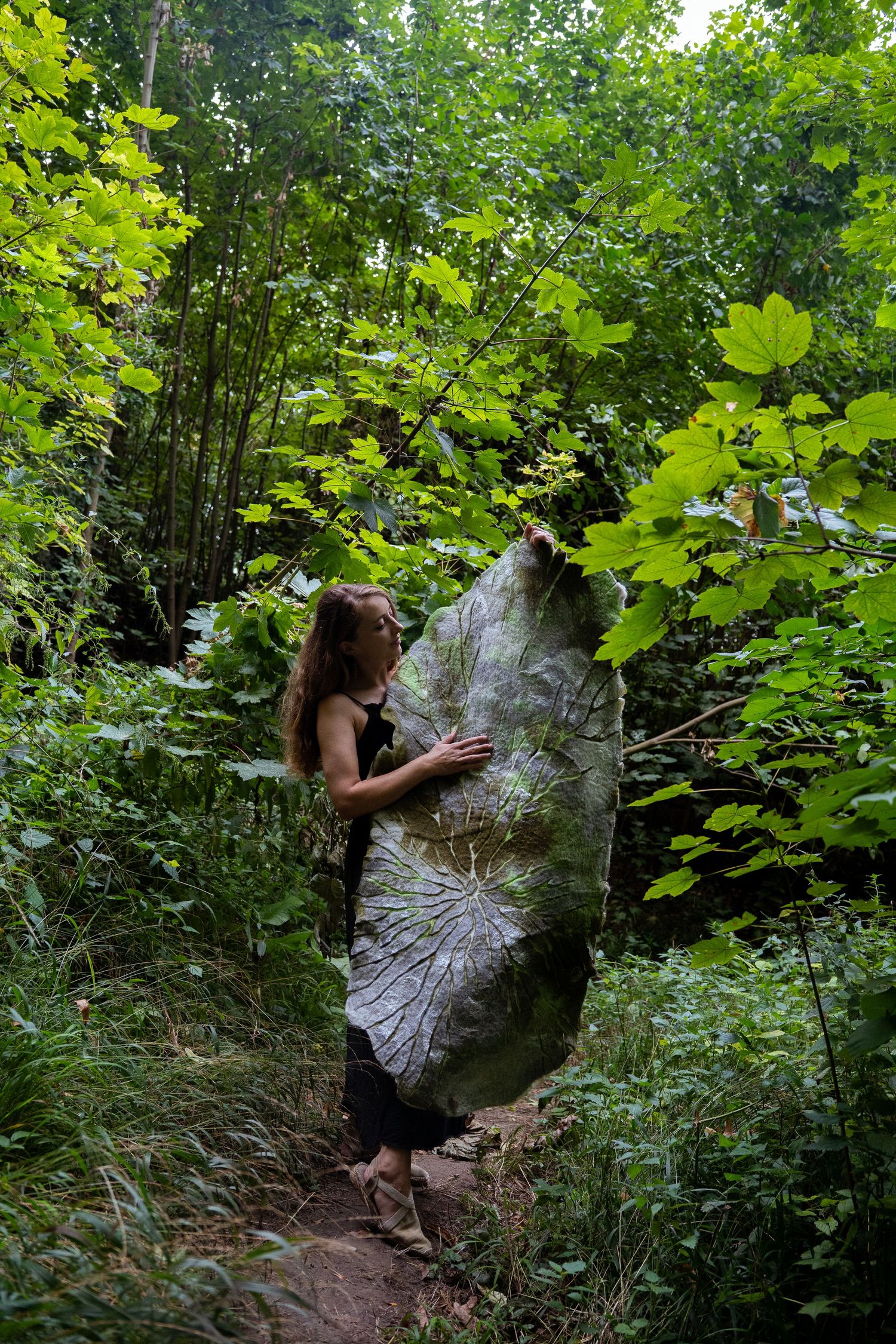 Woman holding large nature-printed textile artwork on a woodland forest path.