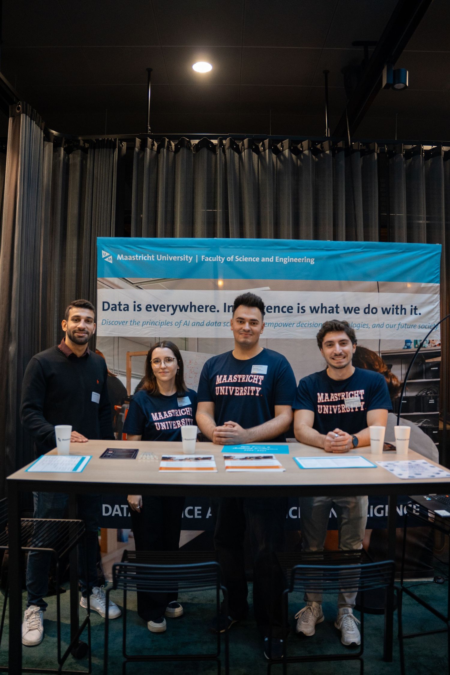 Four students at a Maastricht University Faculty of Science and Engineering booth display data intelligence information.