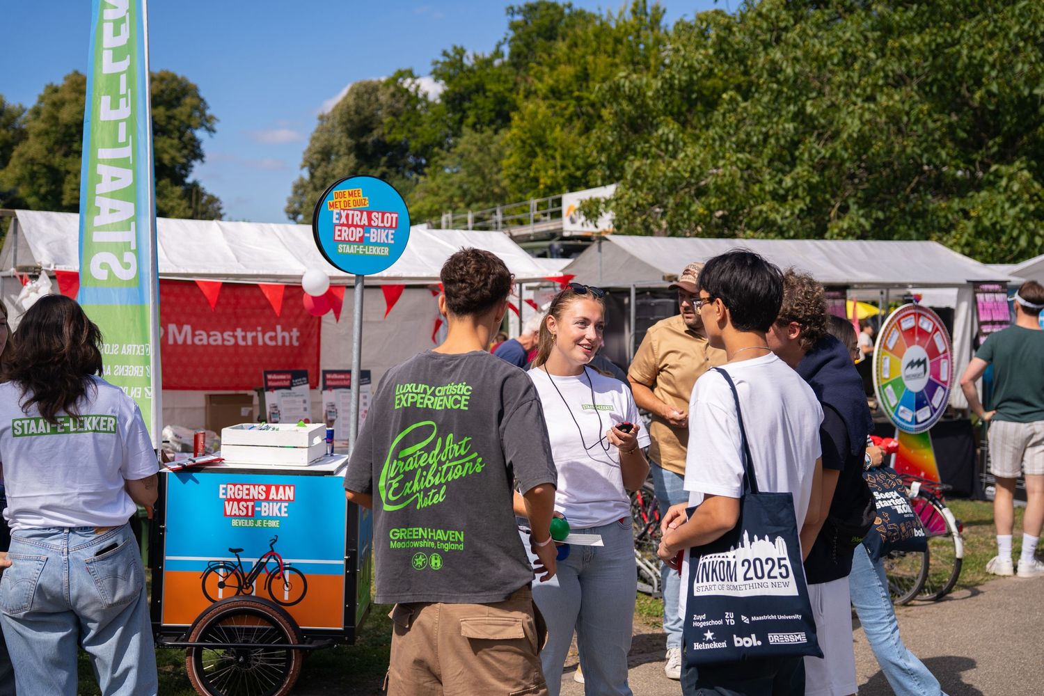 Students socializing at outdoor INKOM 2025 university orientation fair with food vendors.