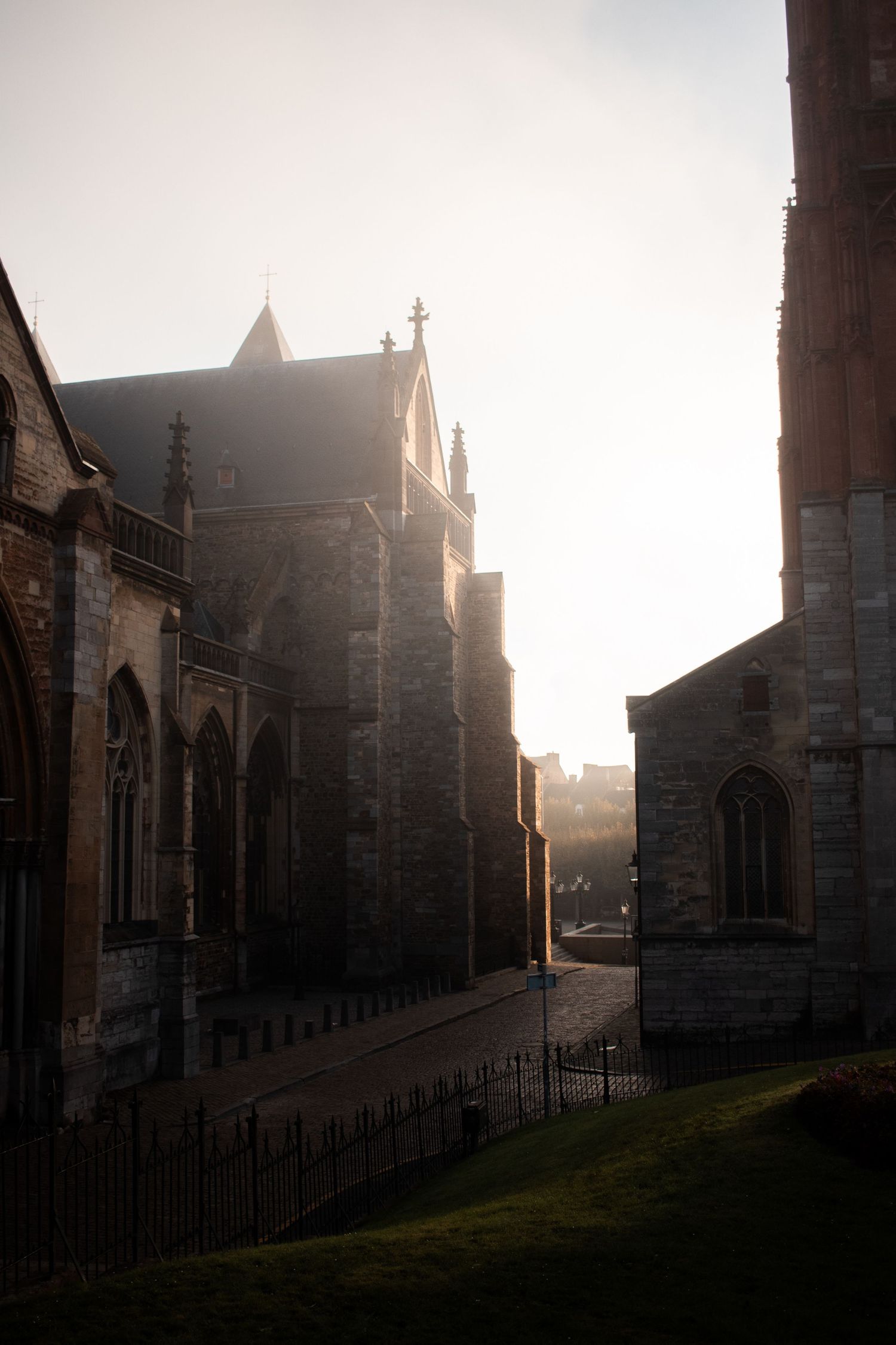 Misty morning light illuminating a historic stone church and cobblestone street in an old European city.