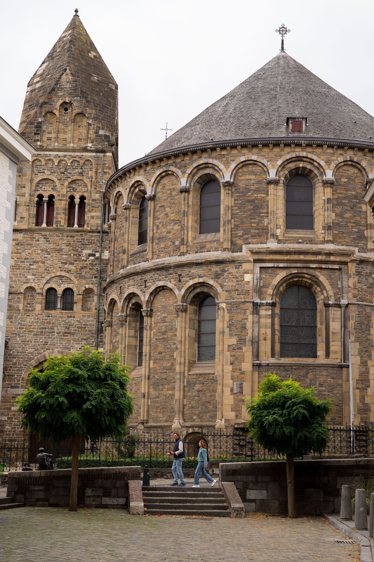 Romanesque church with ornate apse and stone bell tower in a European city square with visitors.