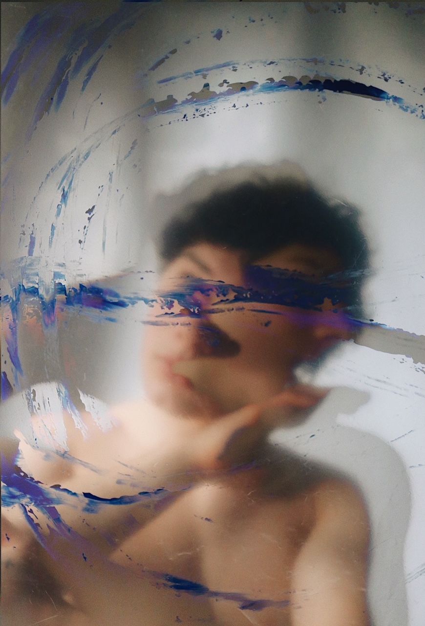Blurred artistic portrait of a person behind glass smeared with blue and purple paint strokes.