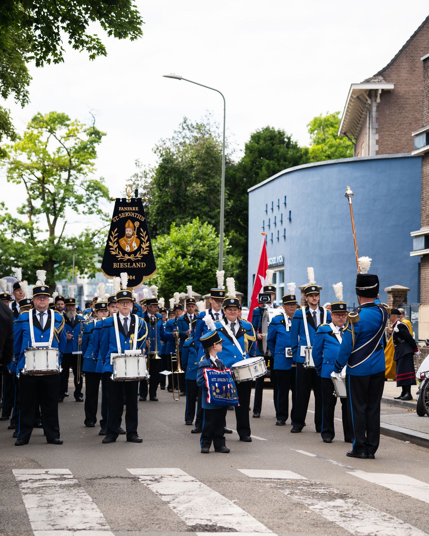 Marching band in blue uniforms with banner parades through town street.