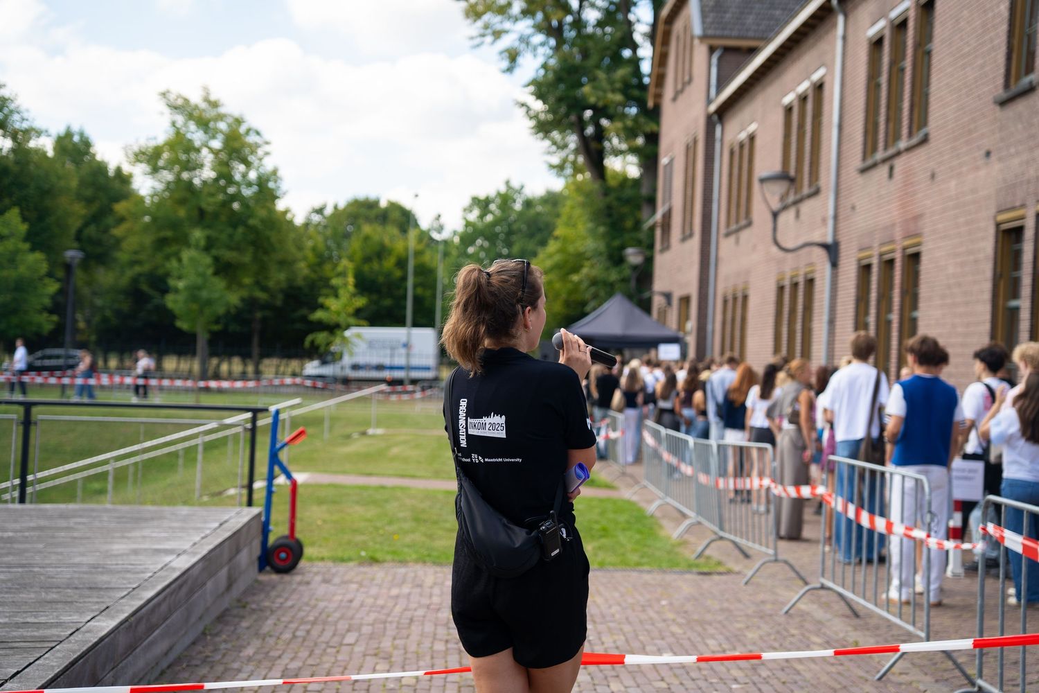 Event staff member in black shirt monitoring queue at outdoor university campus event.