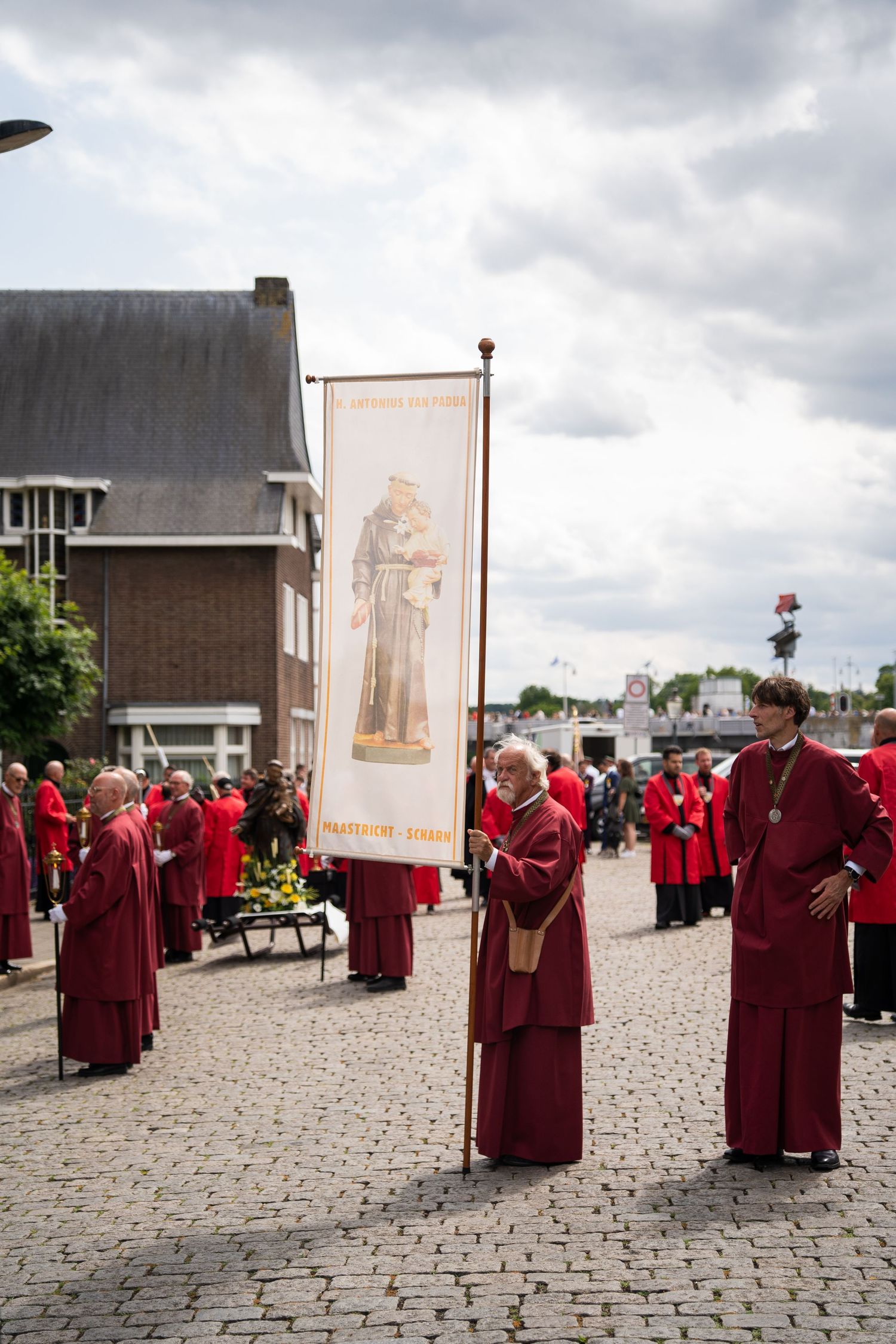 Members of a religious procession in red robes carrying a banner through a cobblestone square in Maastricht.
