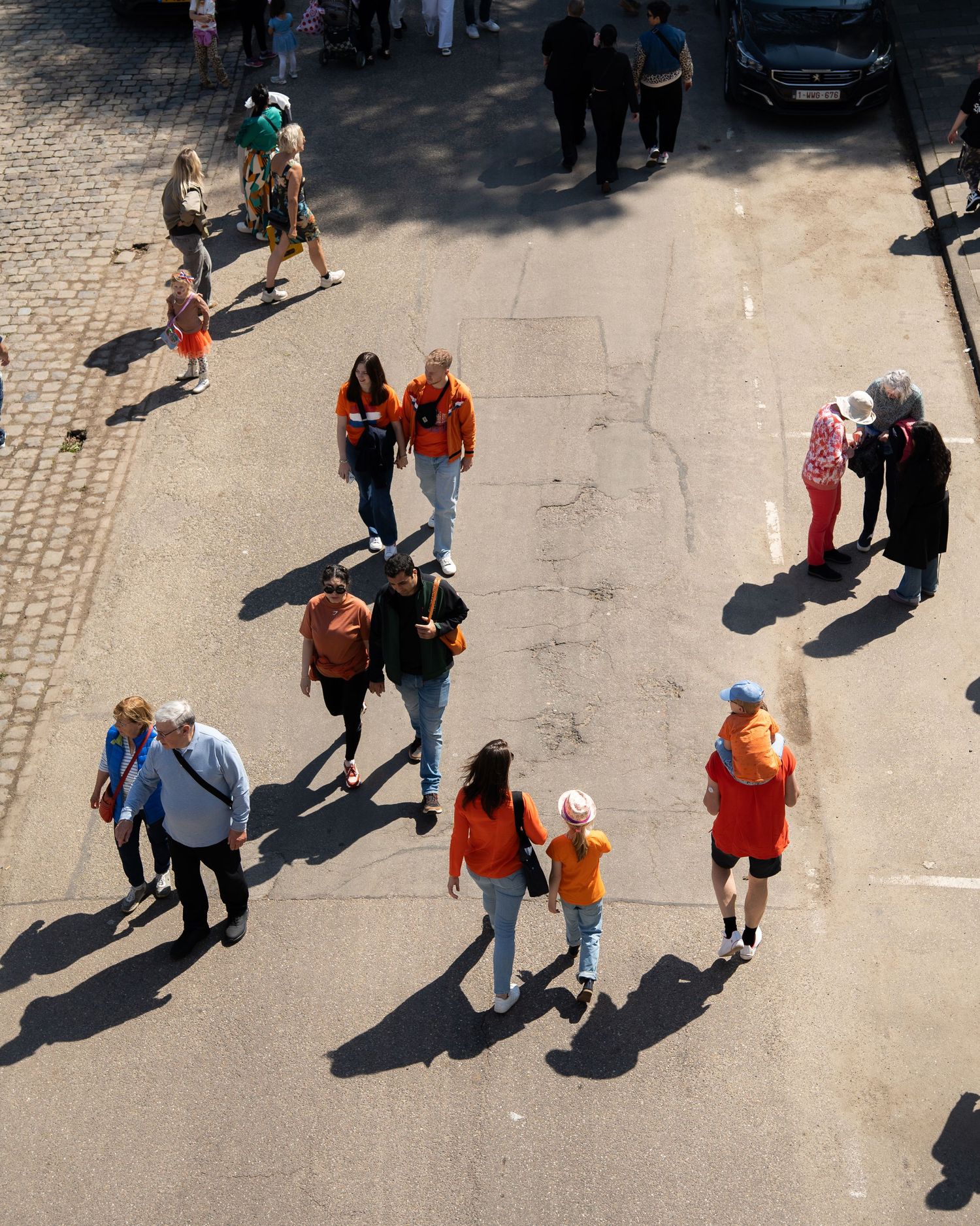 Aerial view of people dressed in orange walking on a sunny cobblestone street during Kings Day in the Netherlands.