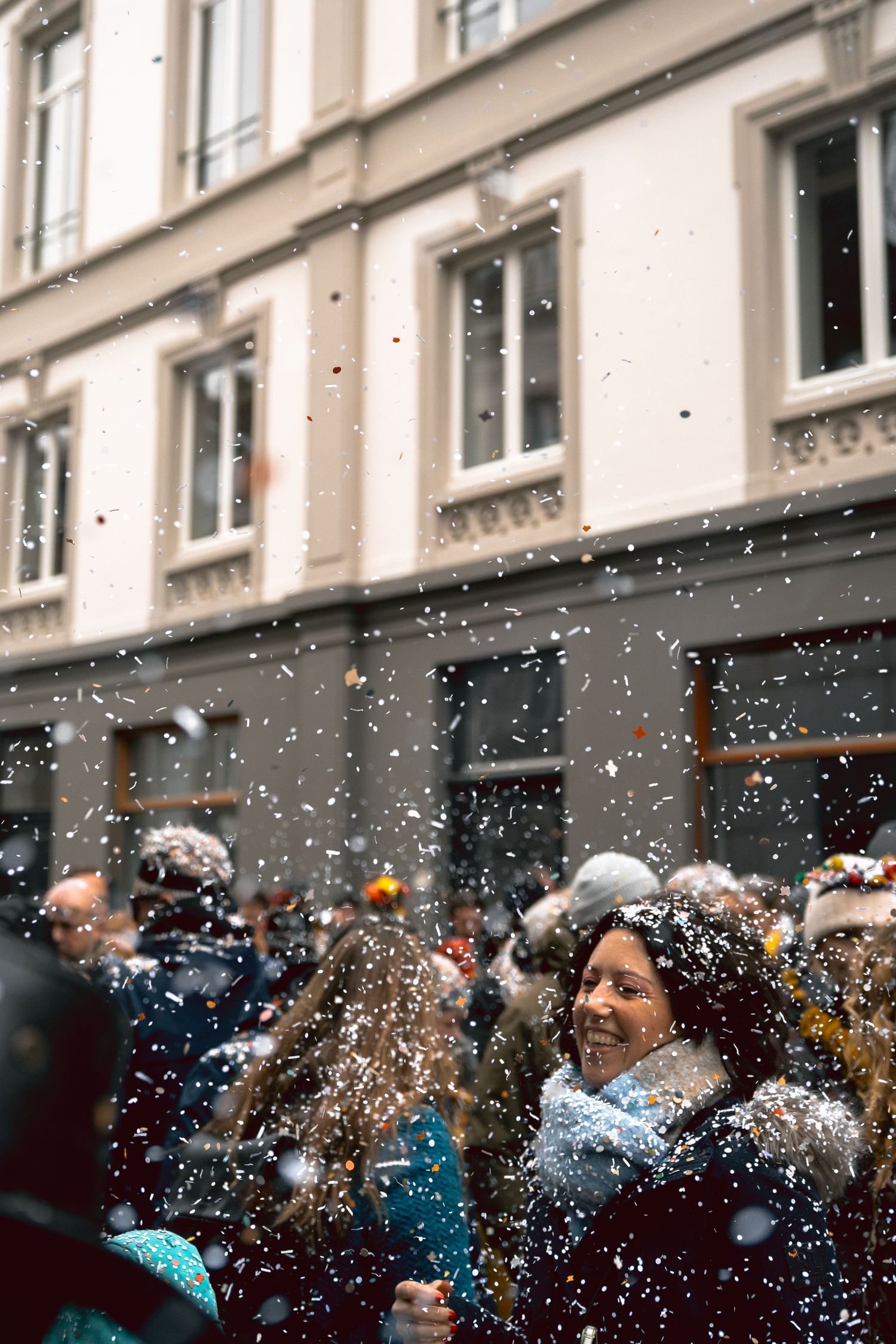 Smiling woman surrounded by falling confetti during a festive street celebration in a city.