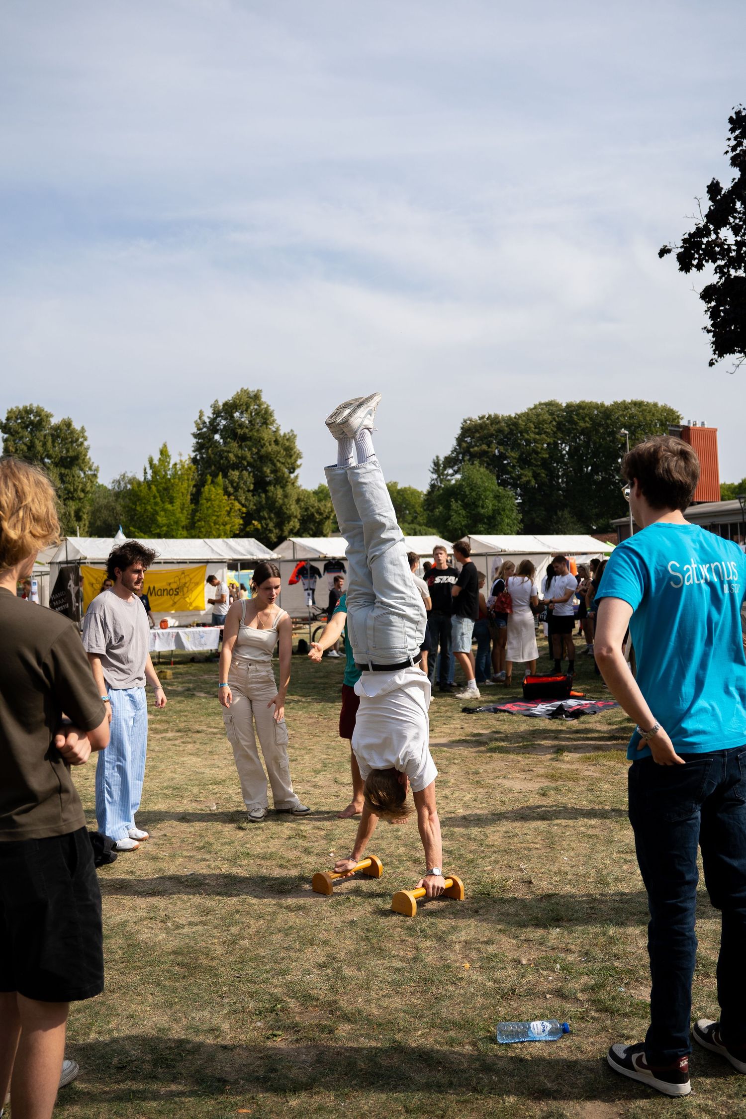 A student performs a handstand on the grass at an outdoor university fair while others watch.