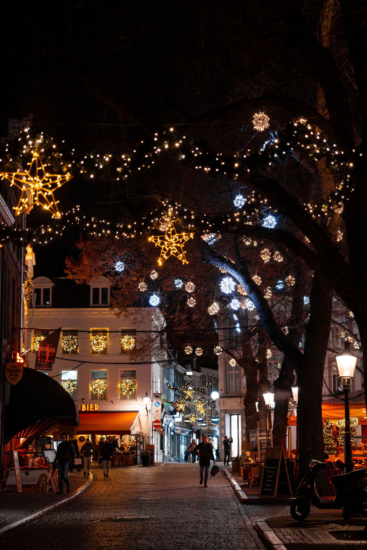 A festive street at night adorned with Christmas lights, snowflake decorations, and glowing stars in a European city.