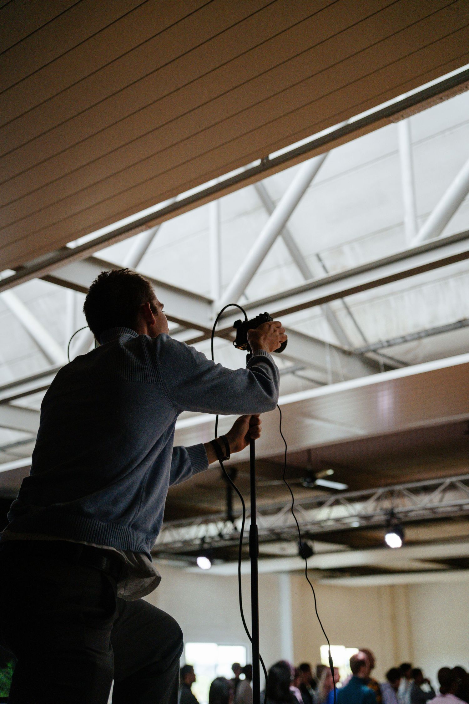 Silhouette of a person holding a microphone on stage facing a crowd in an industrial venue.