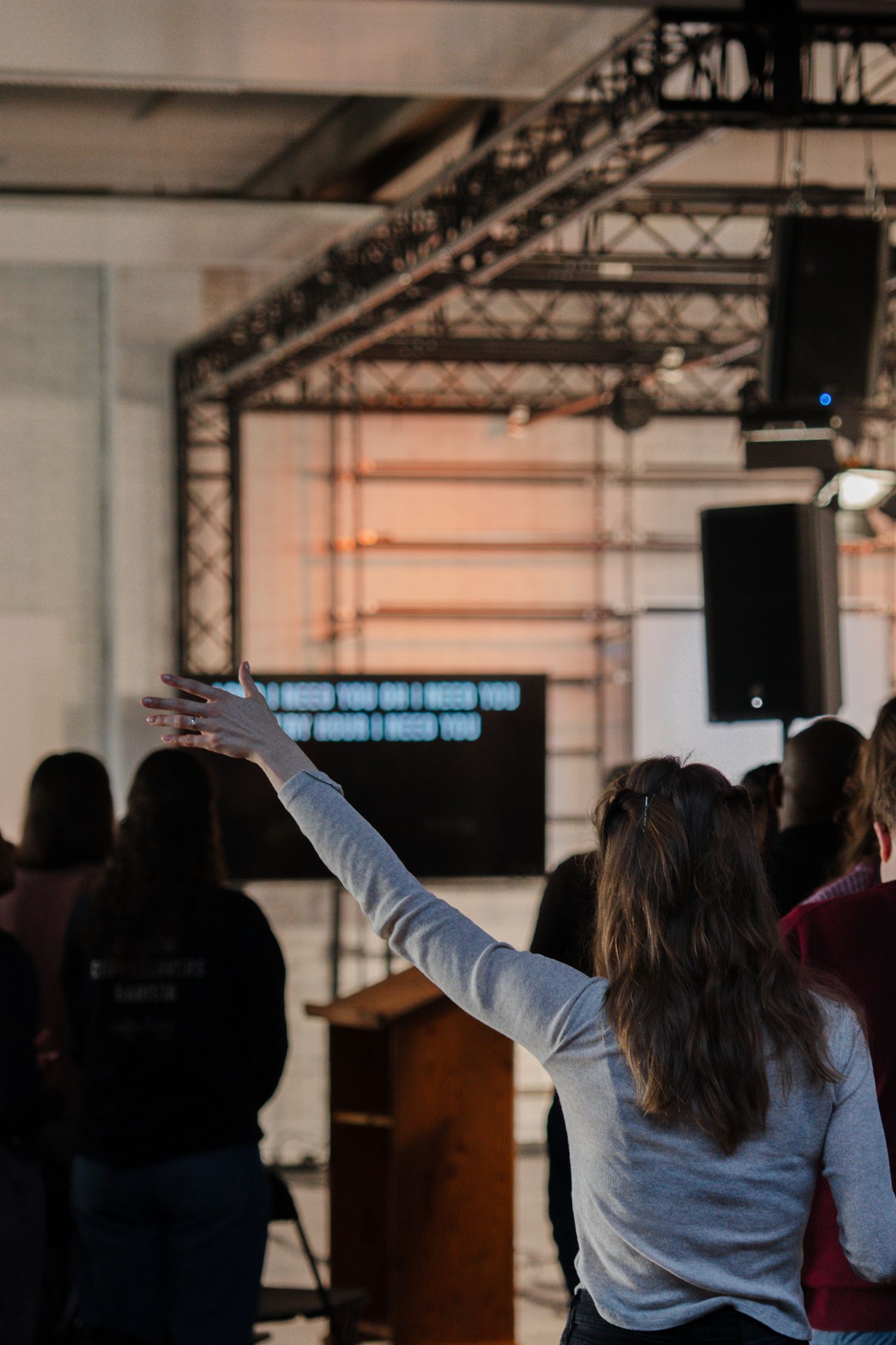 Woman raising her hand in worship toward a church stage displaying song lyrics on a screen.