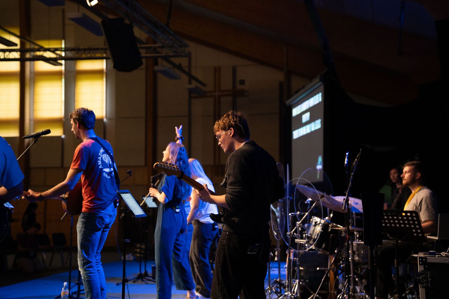 Christian worship band performs on stage with singers and musicians during a church event in an indoor venue.