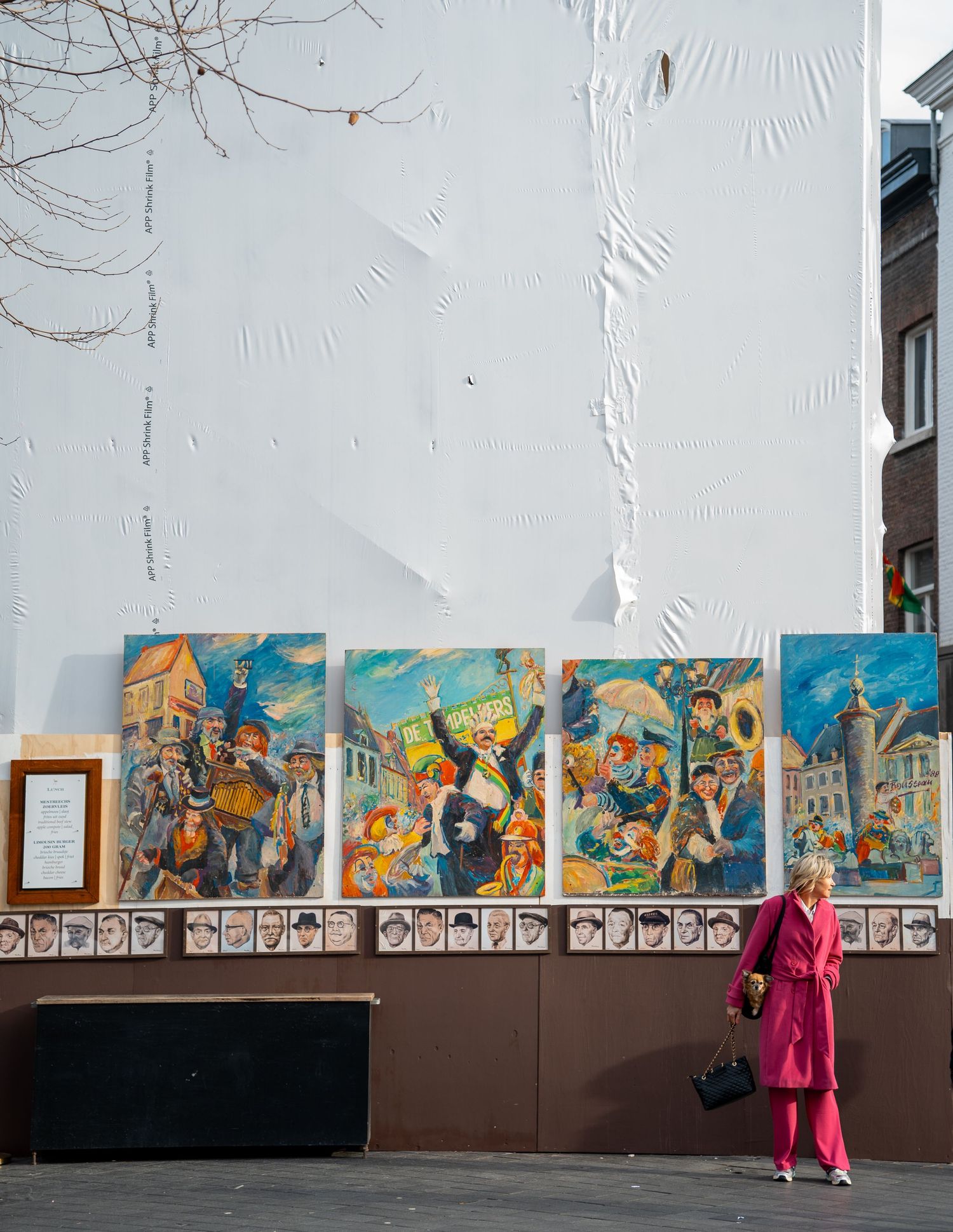 Woman in pink suit viewing colorful street paintings displayed on a white wall in an urban setting.