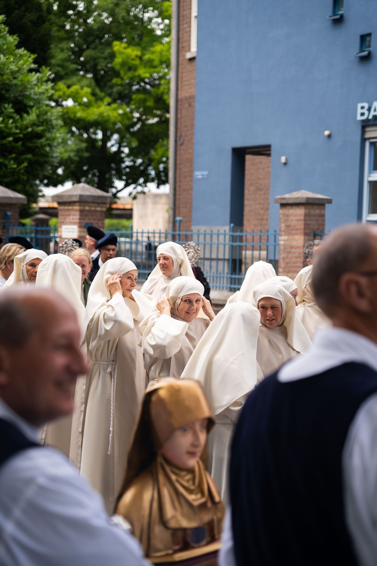 Nuns in white habits adjust veils during outdoor Catholic religious procession.