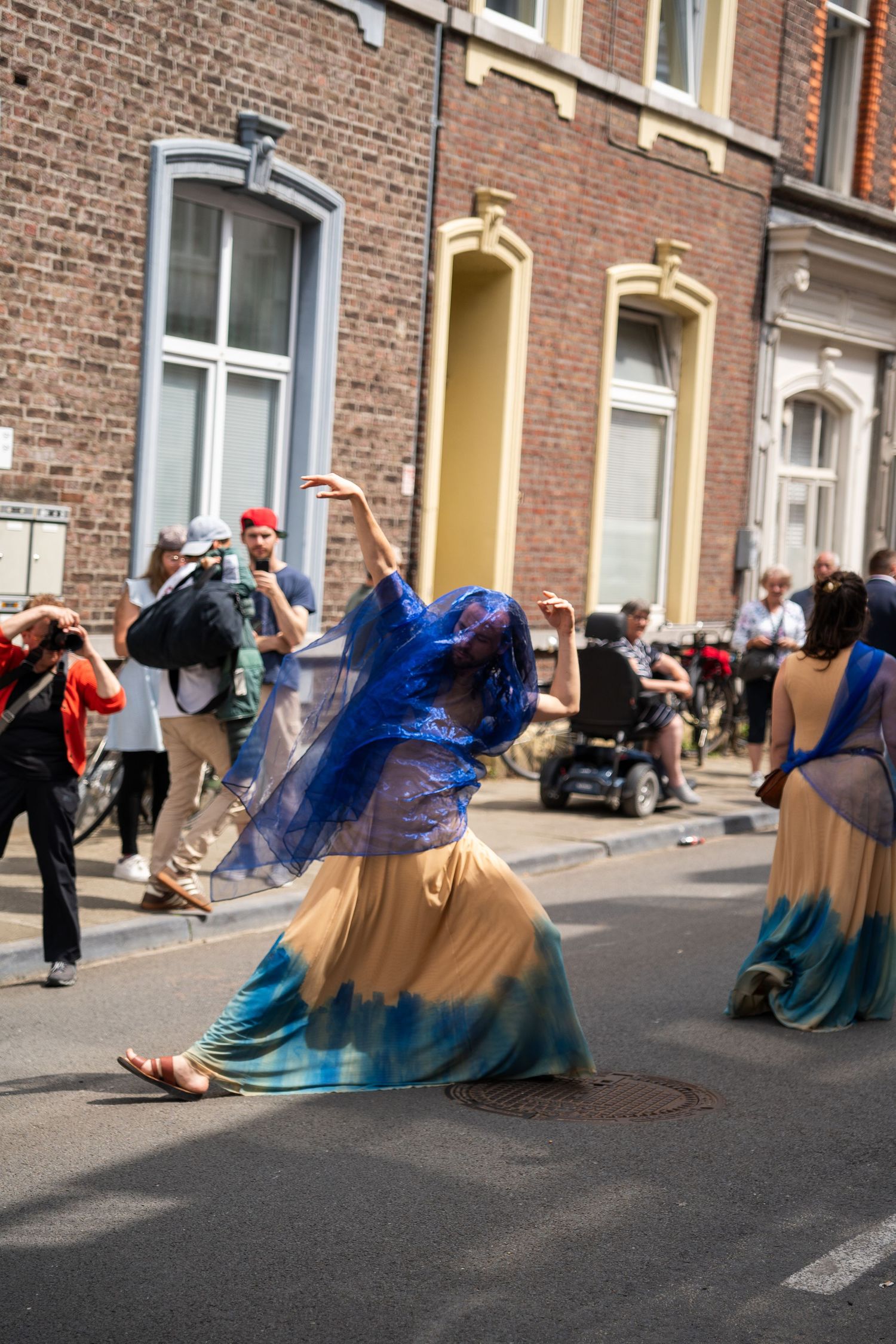 Woman in blue veil and flowing dress performs a dance during an outdoor street festival.
