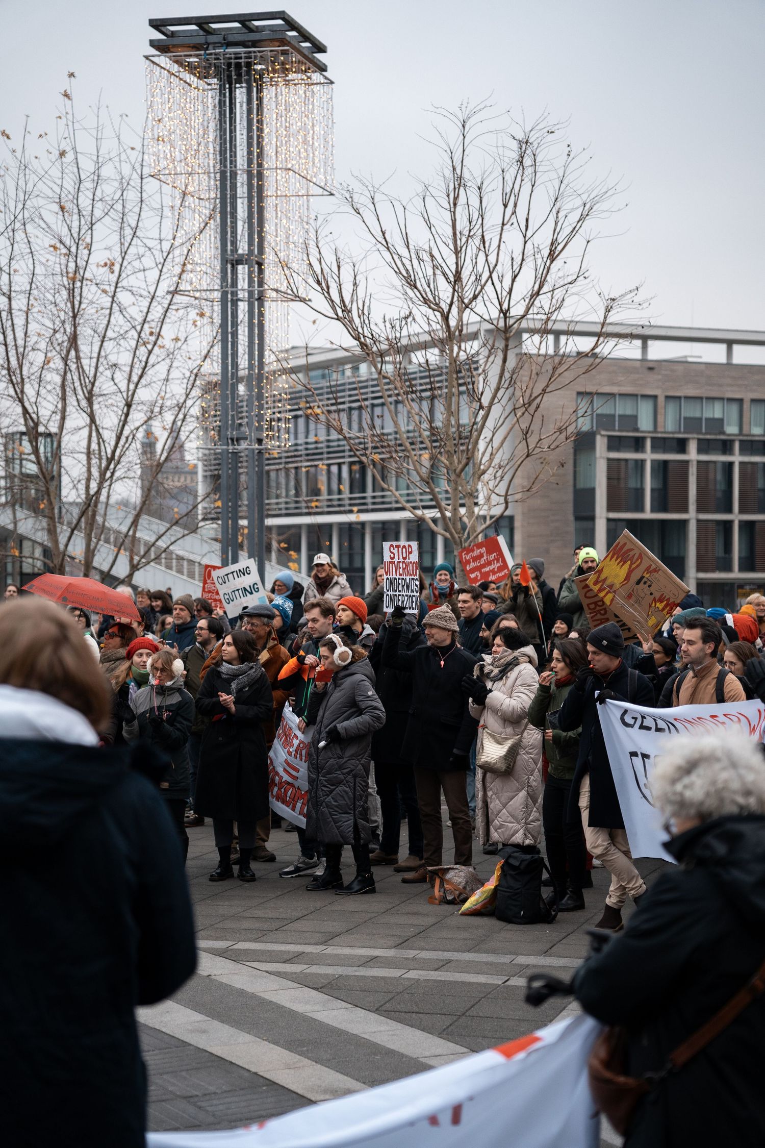 Large crowd of protesters with signs rally in a city square against education budget cuts.