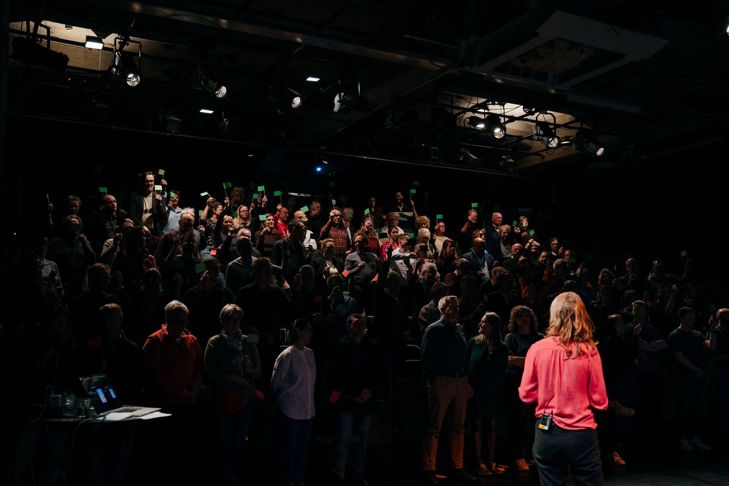 Speaker addresses a large crowd in a darkened theater venue during a live event presentation.