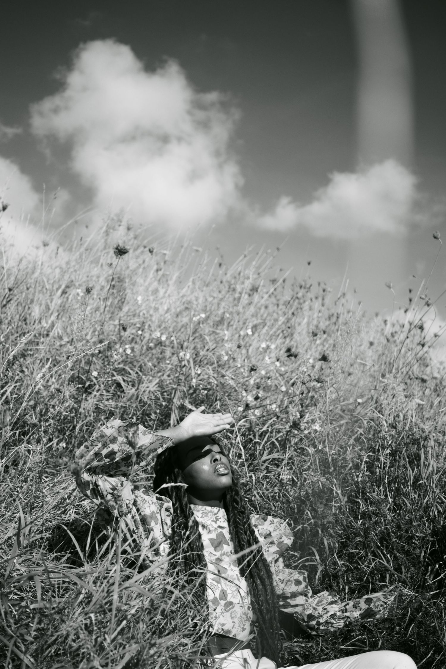 Black and white image of braided woman relaxing in a wildflower meadow under dramatic cloudy sky.