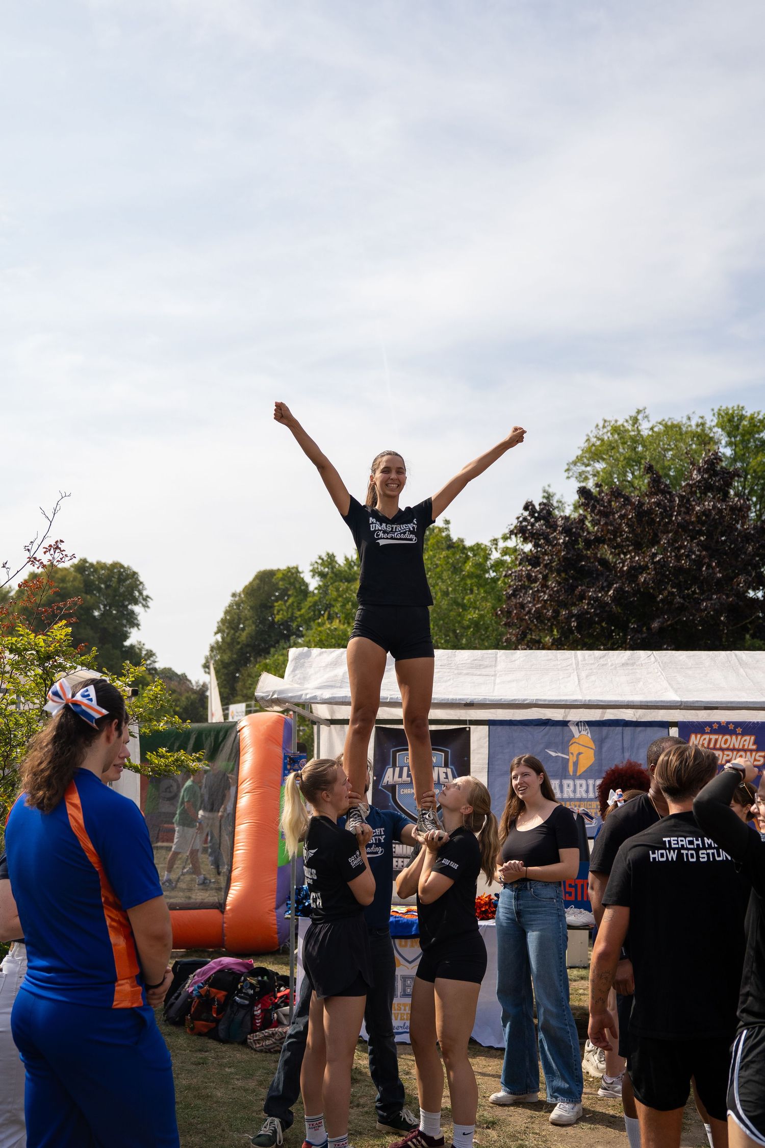 A cheerleader is lifted into a stunt pose by teammates at an outdoor university activities fair.