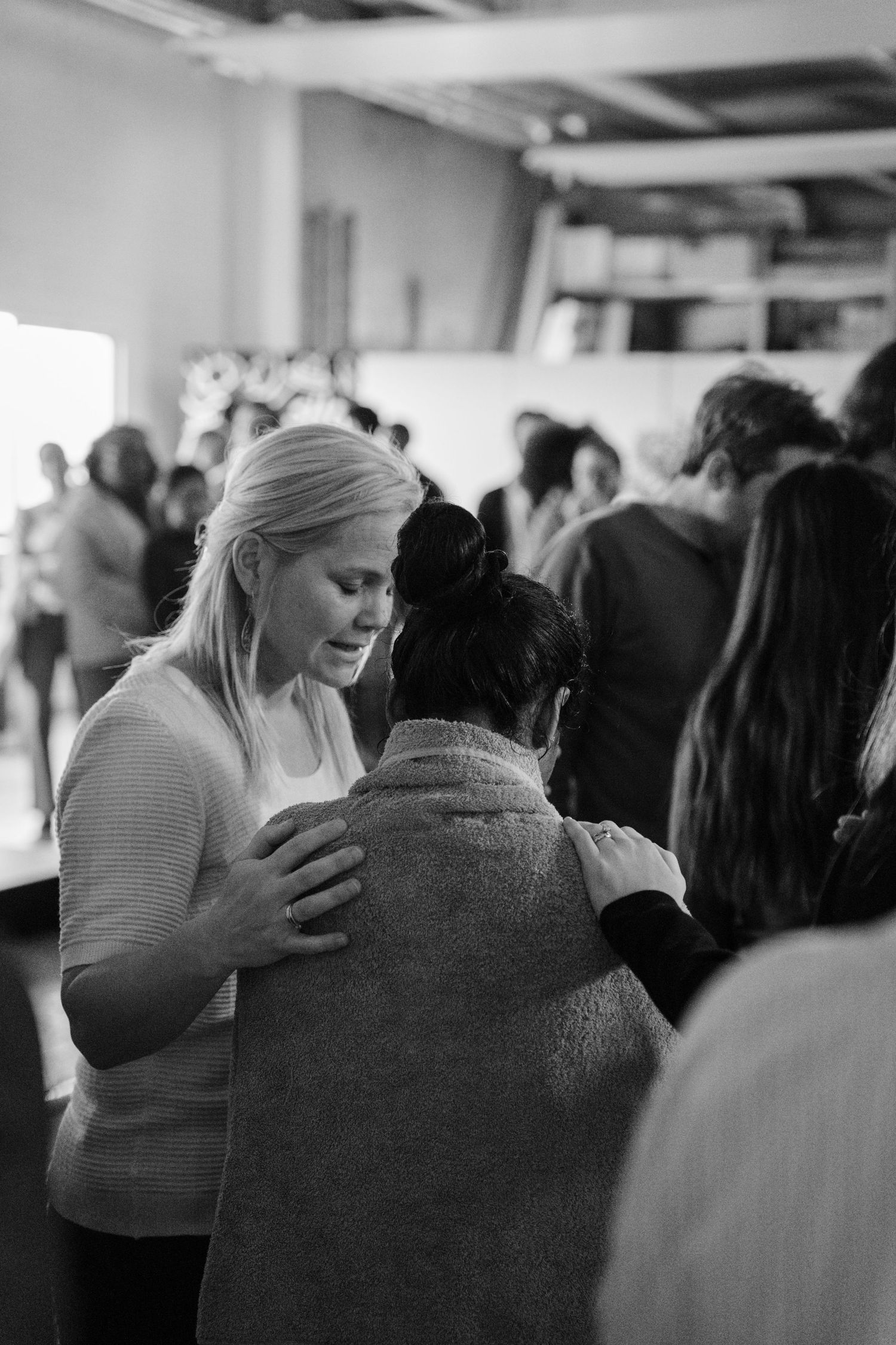 Black and white image of a blonde woman praying with her hand on another persons shoulder during worship.