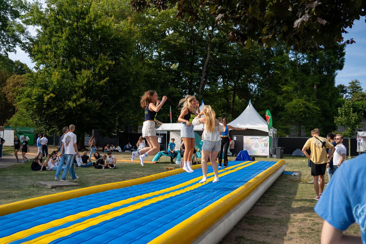 Group of young women jumping together on a large inflatable air track at a sunny outdoor festival.