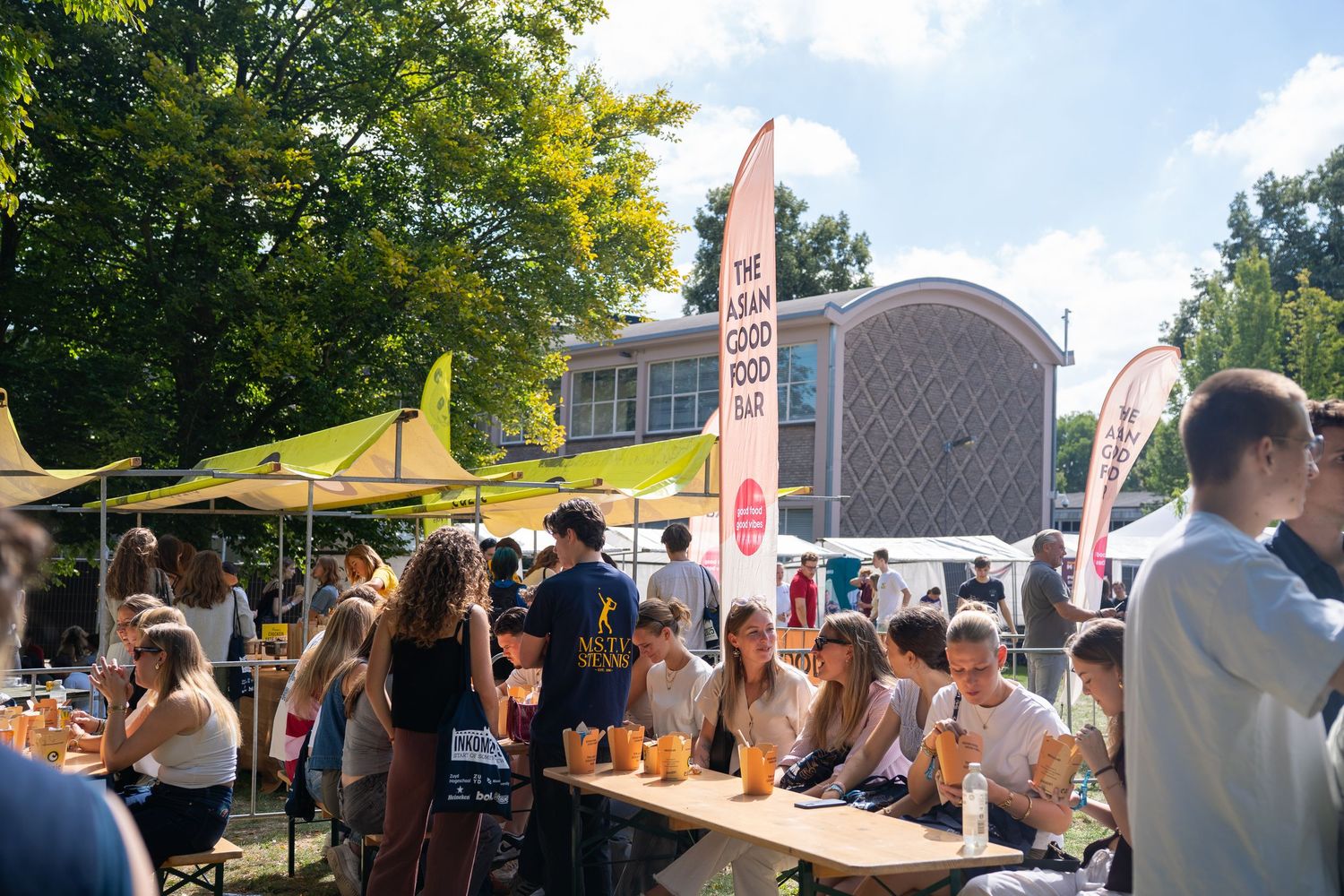 Students enjoying drinks at outdoor tables during sunny INKOM university orientation festival.