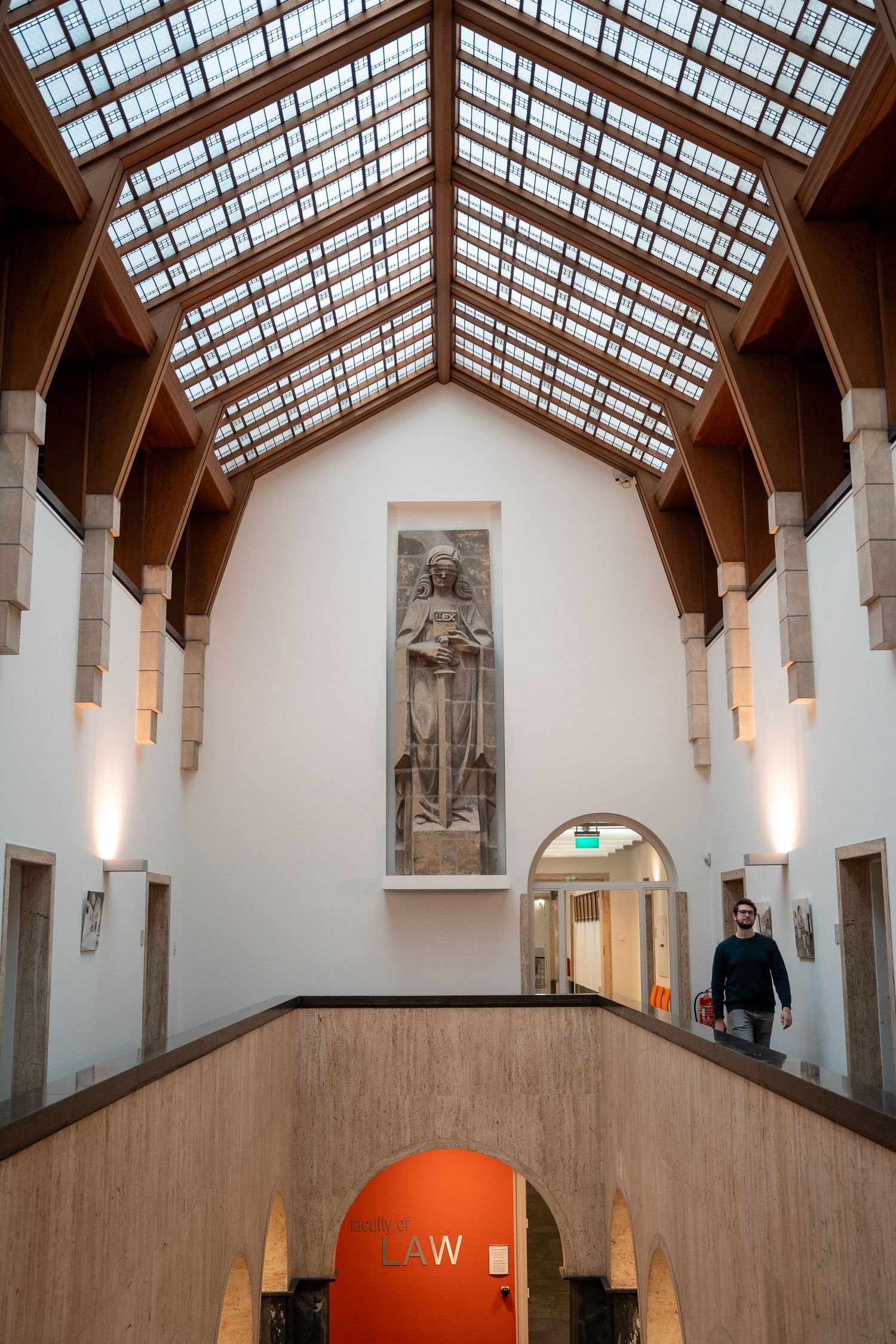Grand university law faculty entrance hall featuring a stone sculpture under a wooden vaulted skylight.