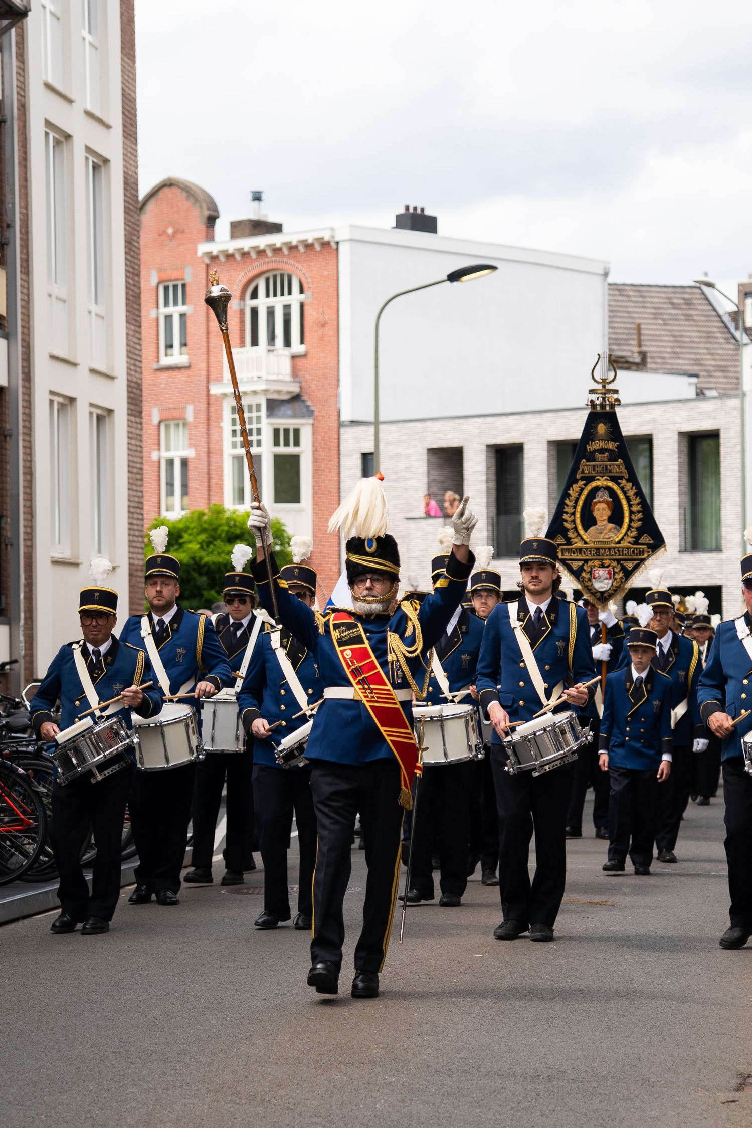 Marching band in blue uniforms led by a drum major parades through a city street.