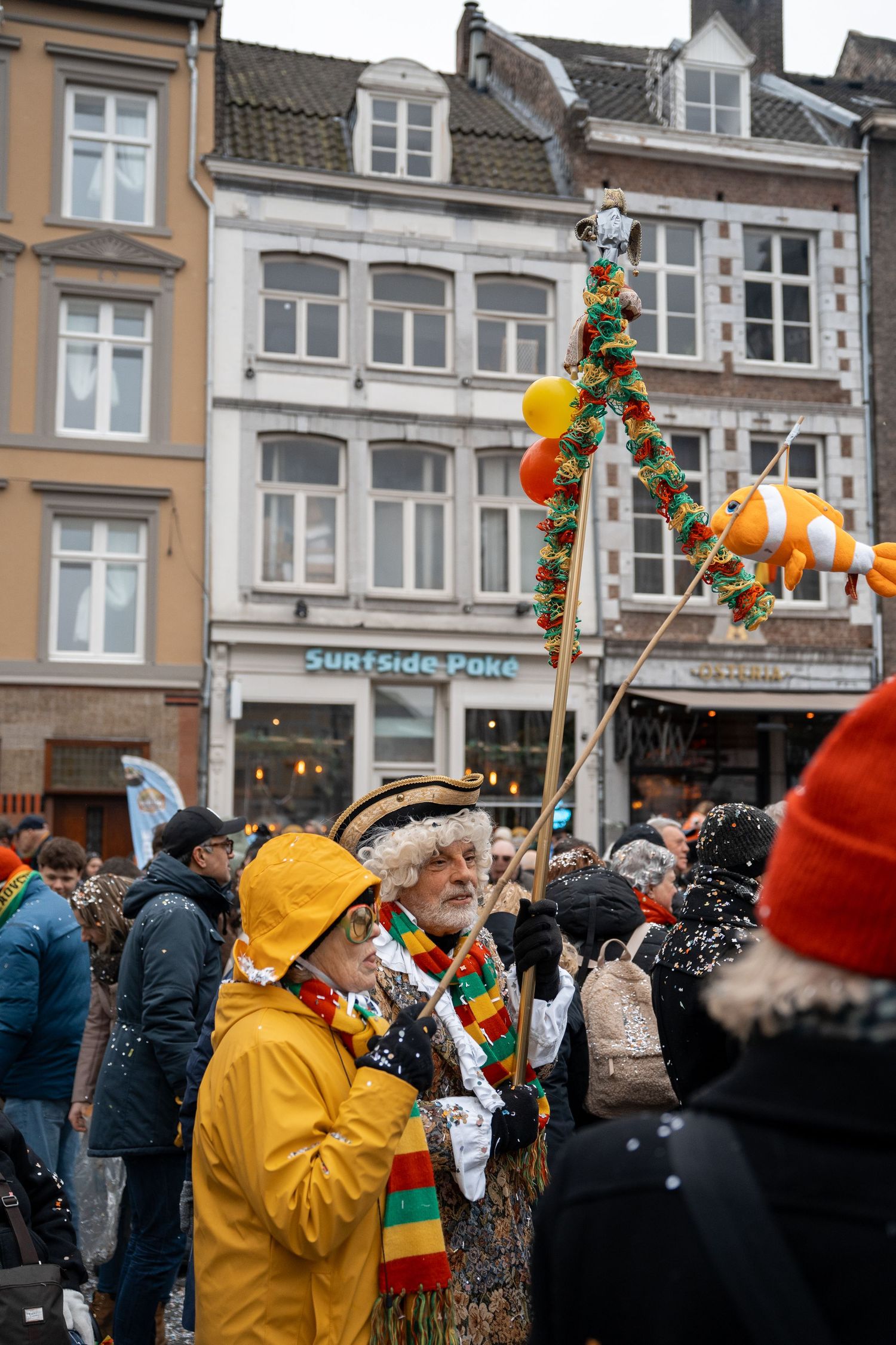 Festive carnival parade participant in yellow raincoat holding a decorated pole with colorful ornaments.