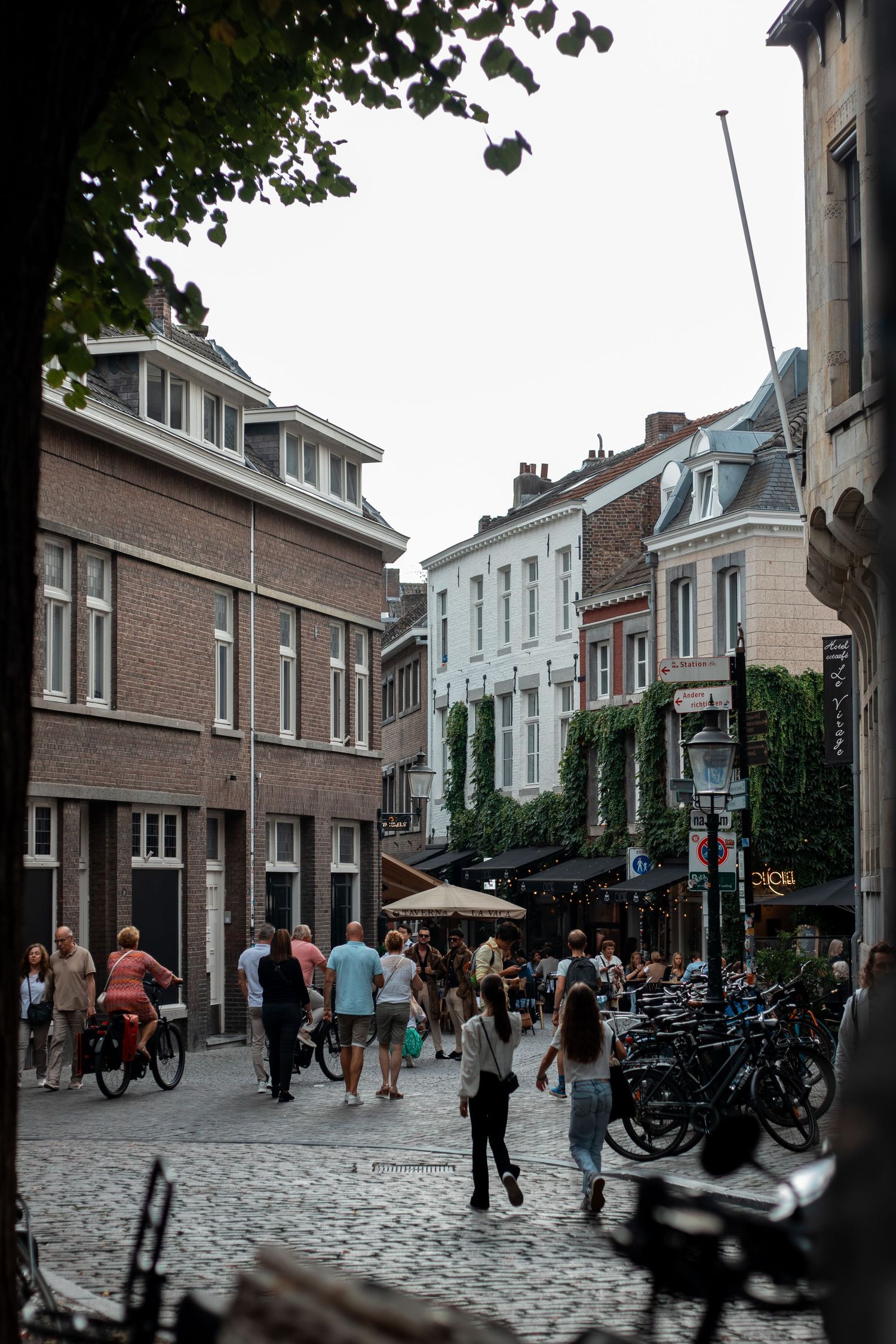 Tourists and locals walking through a bustling cobblestone street lined with brick buildings and outdoor cafes in Maastricht.