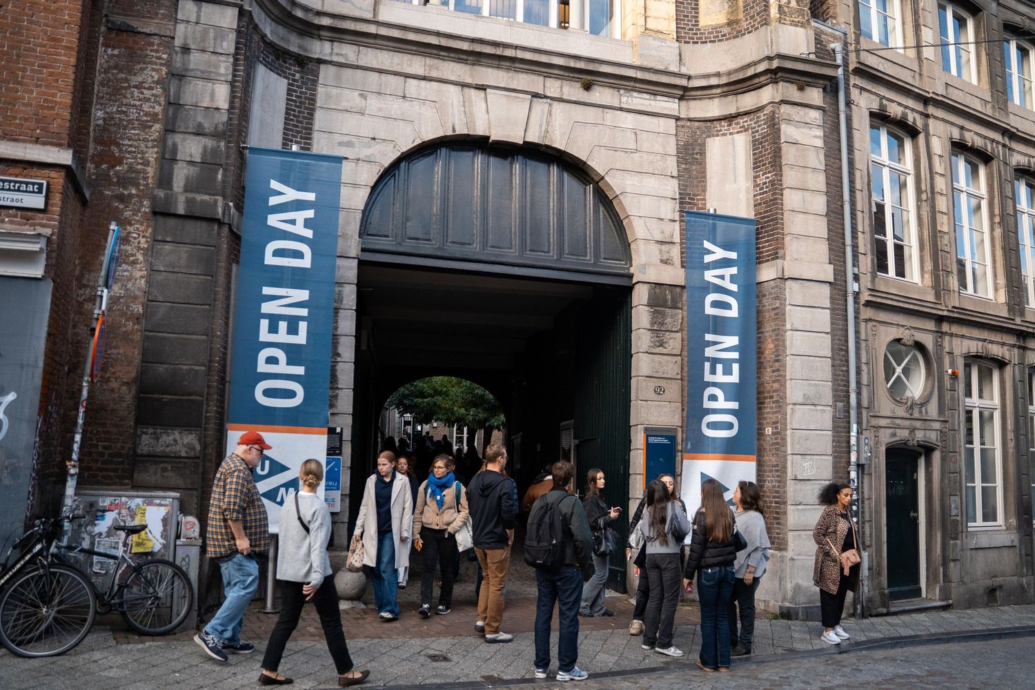 Visitors walk through a historic arched gateway decorated with Open Day banners at Maastricht University.