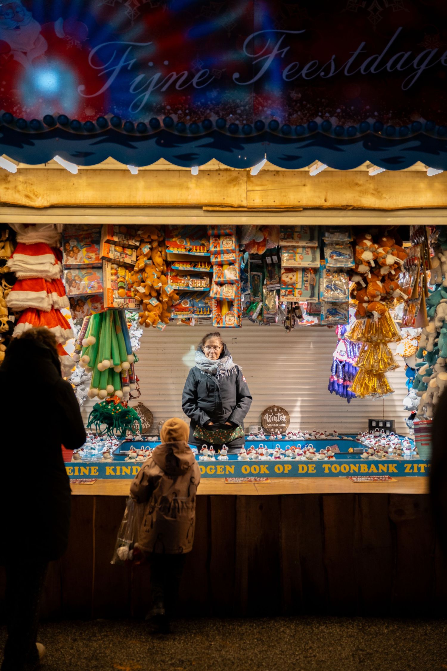 Colorful toy stall at a Christmas market with a vendor standing behind the counter displaying festive merchandise.