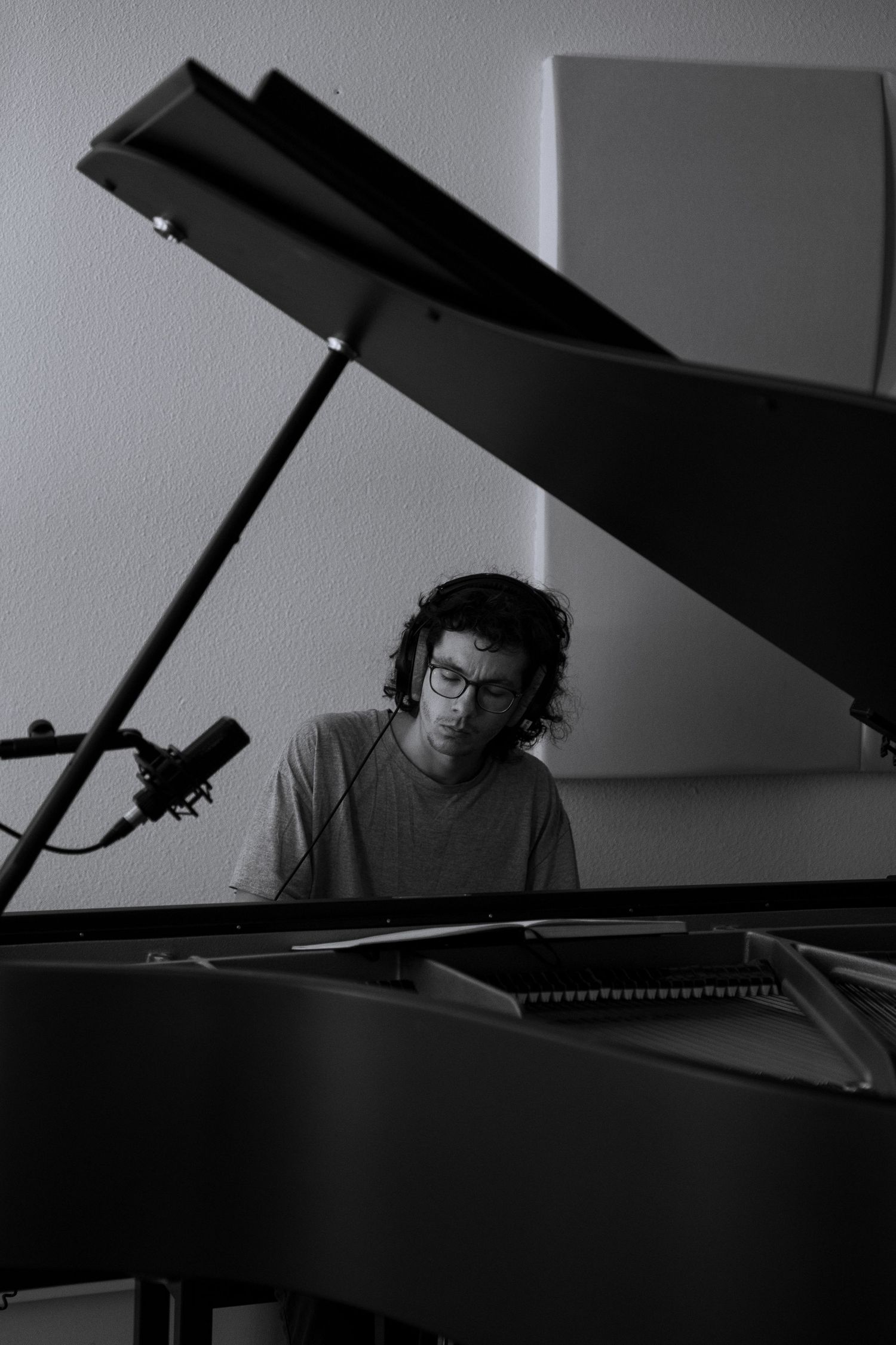 Black and white photo of a man with glasses playing a grand piano in a recording studio.