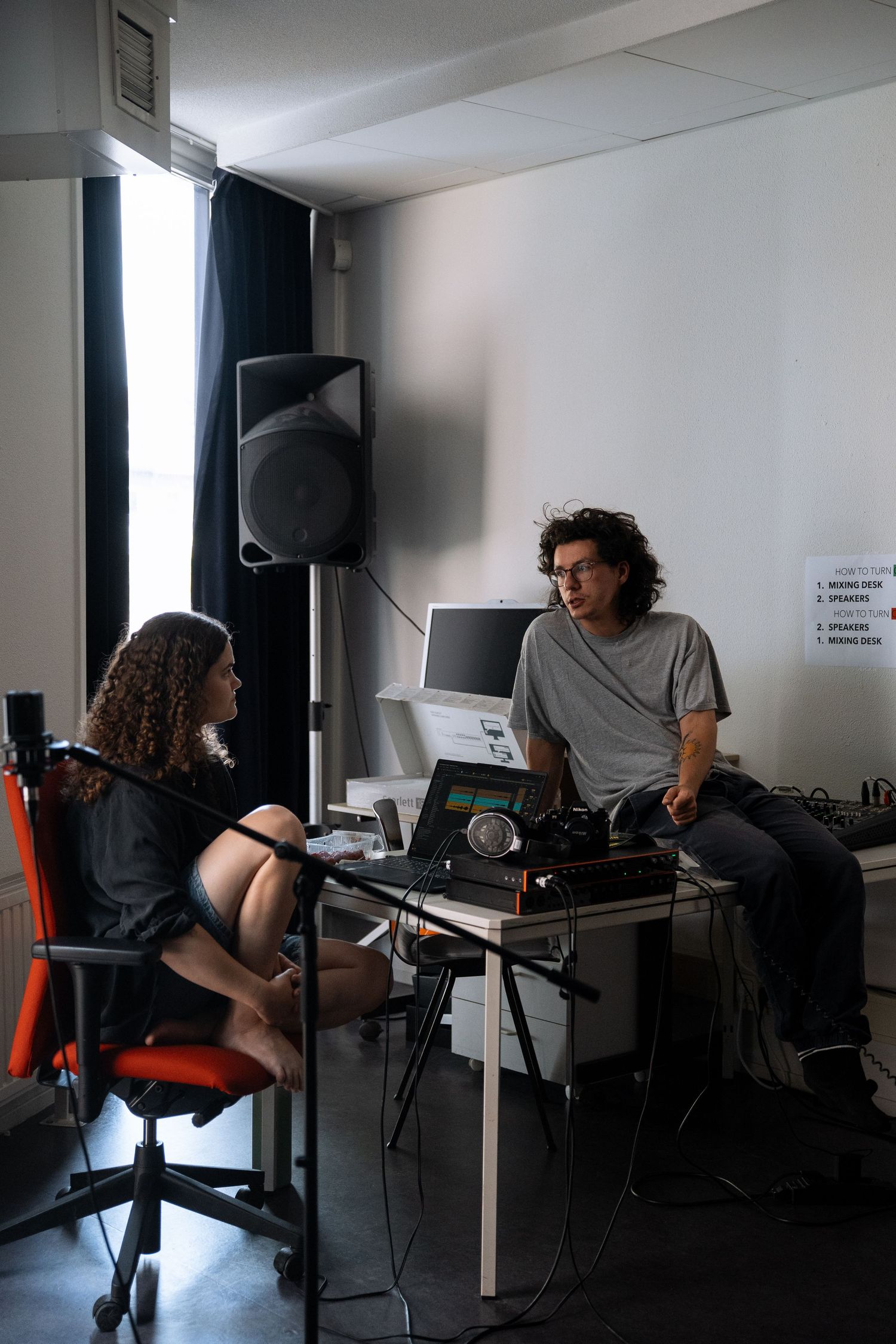 Two musicians discuss music production at a recording studio workstation with equipment.